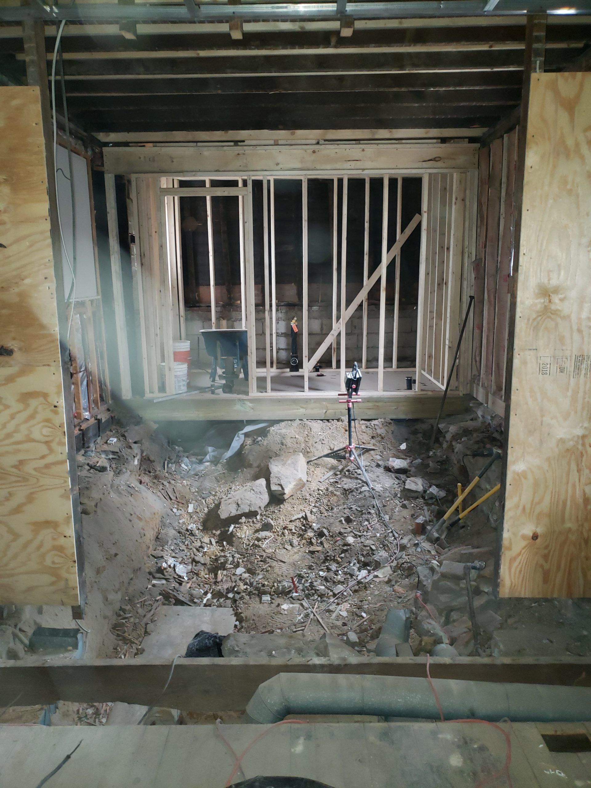Construction site: doorway framed with wood studs and plywood. Debris on floor.