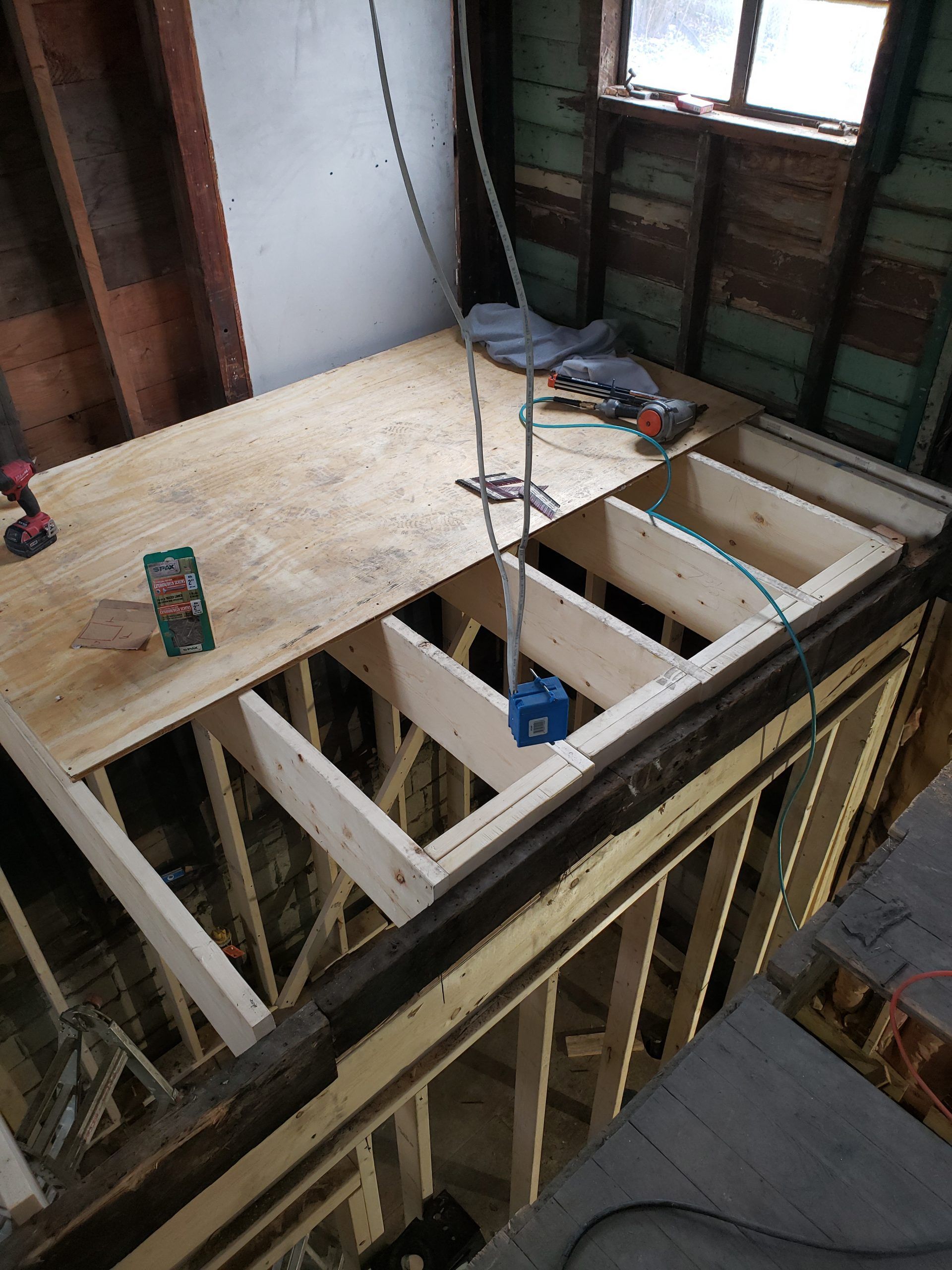 Construction of a small loft space with plywood floor and exposed wooden beams; electrical wiring visible.