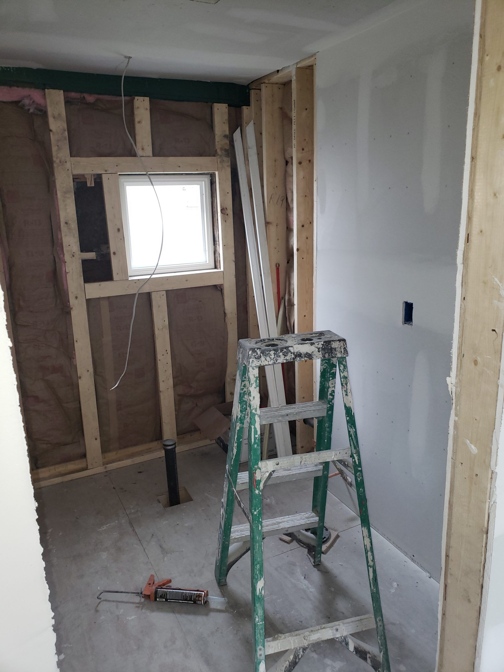 Bathroom under construction; framing, insulation, drywall, ladder, tool, window, unfinished.