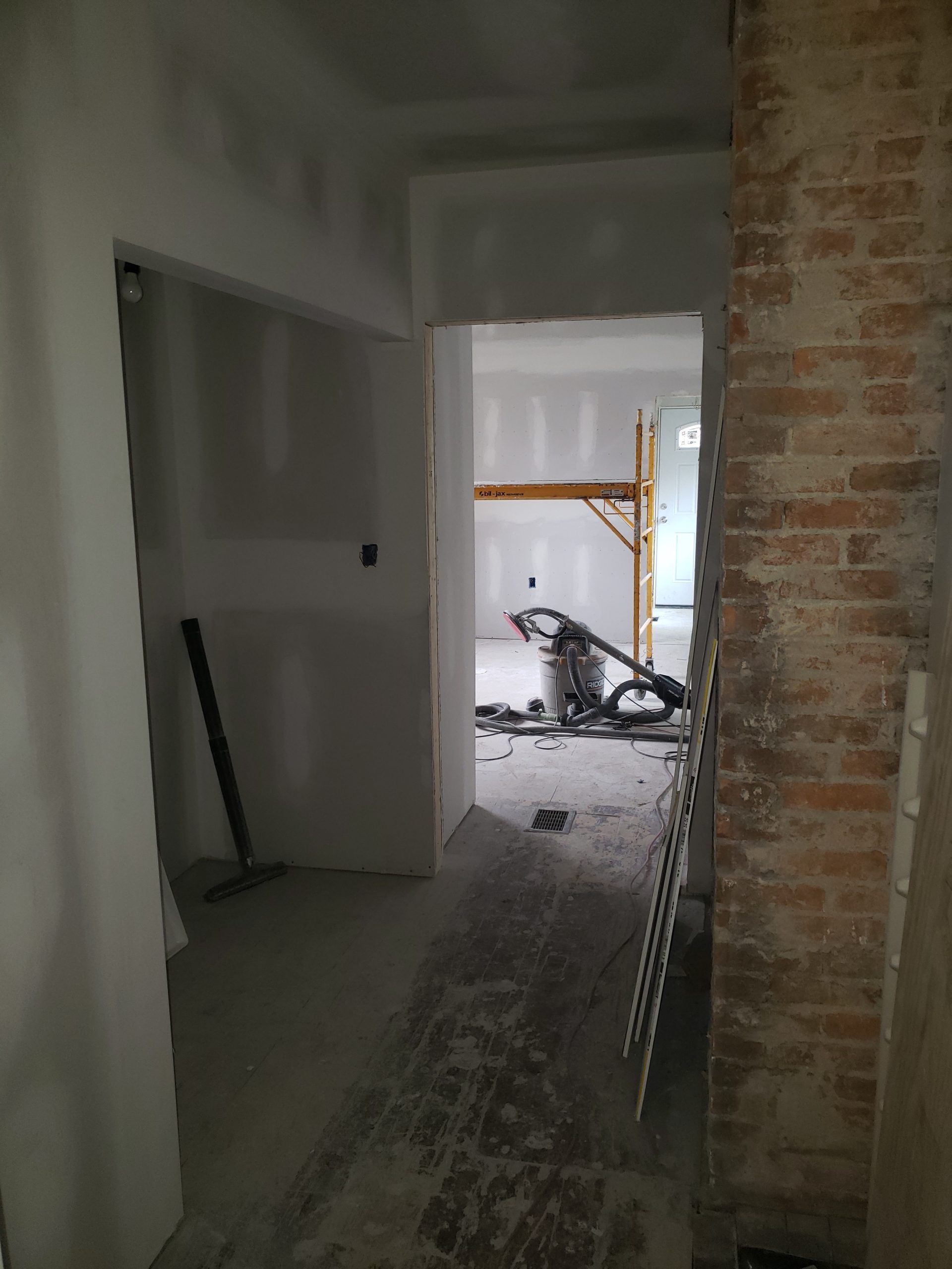 Interior hallway undergoing renovation, with exposed brick, drywall, and construction equipment.