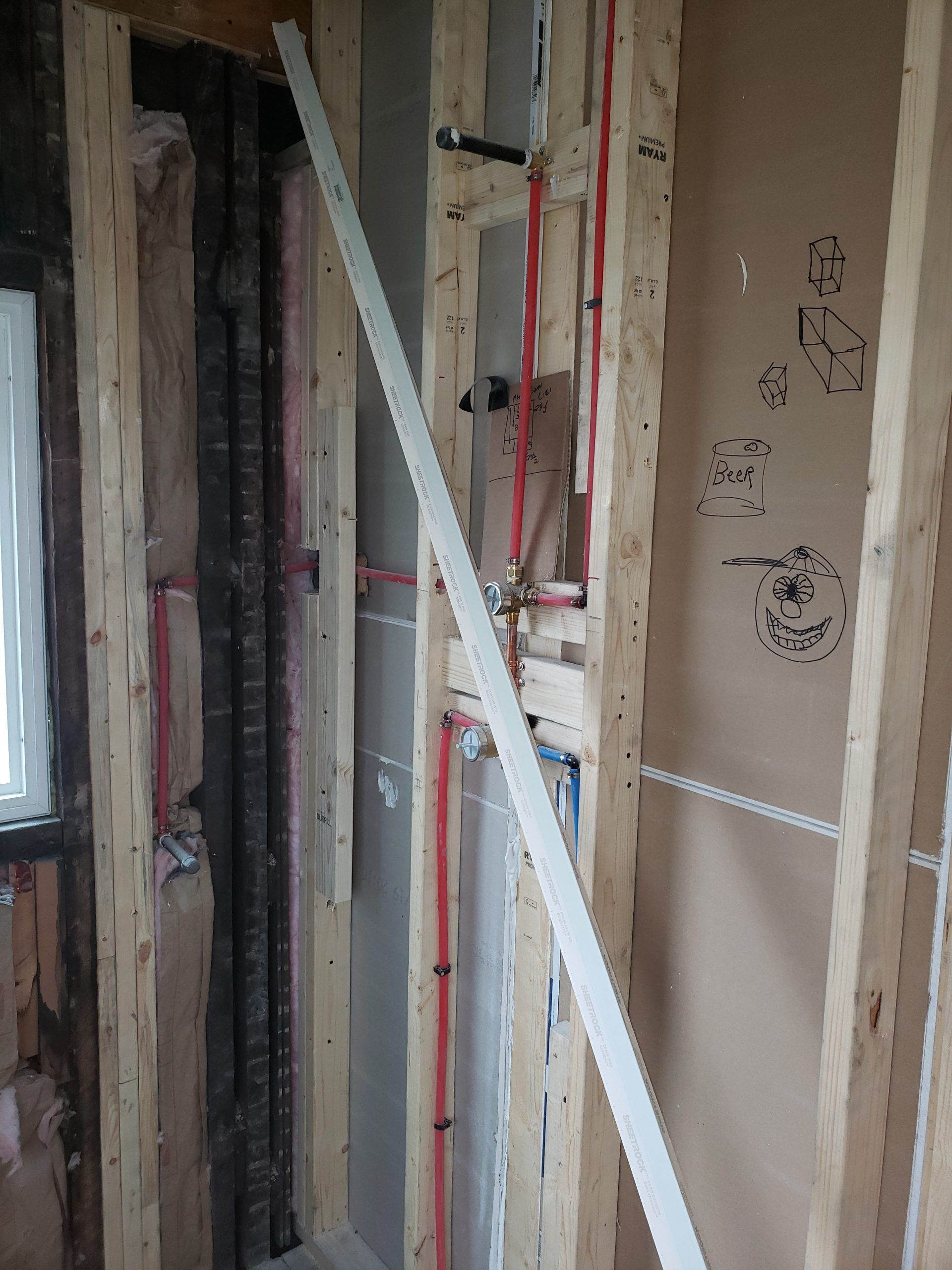Interior wall under construction with exposed plumbing and wooden framing.