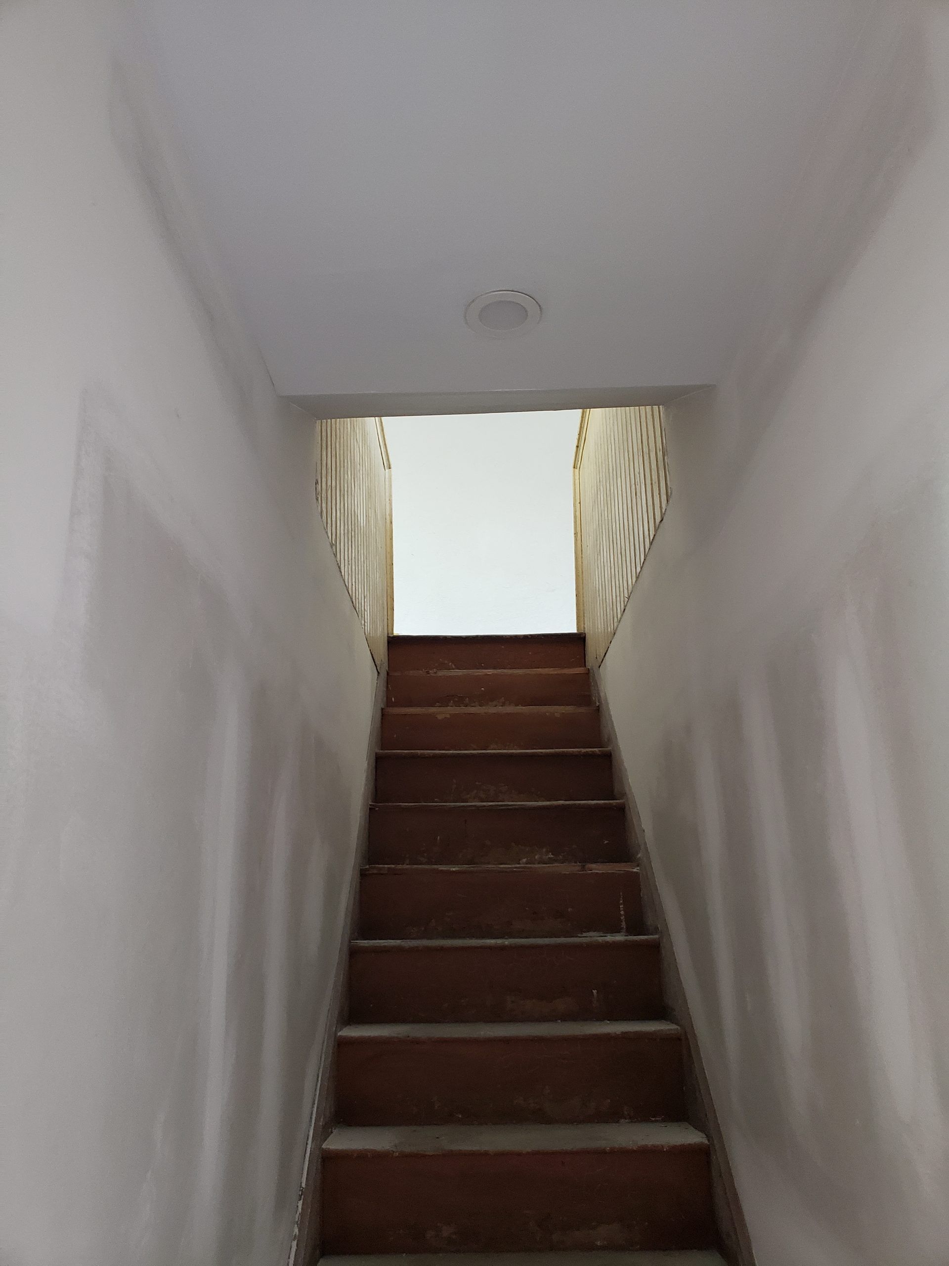 Staircase with wooden steps leading upwards, white walls, and a light at the top.