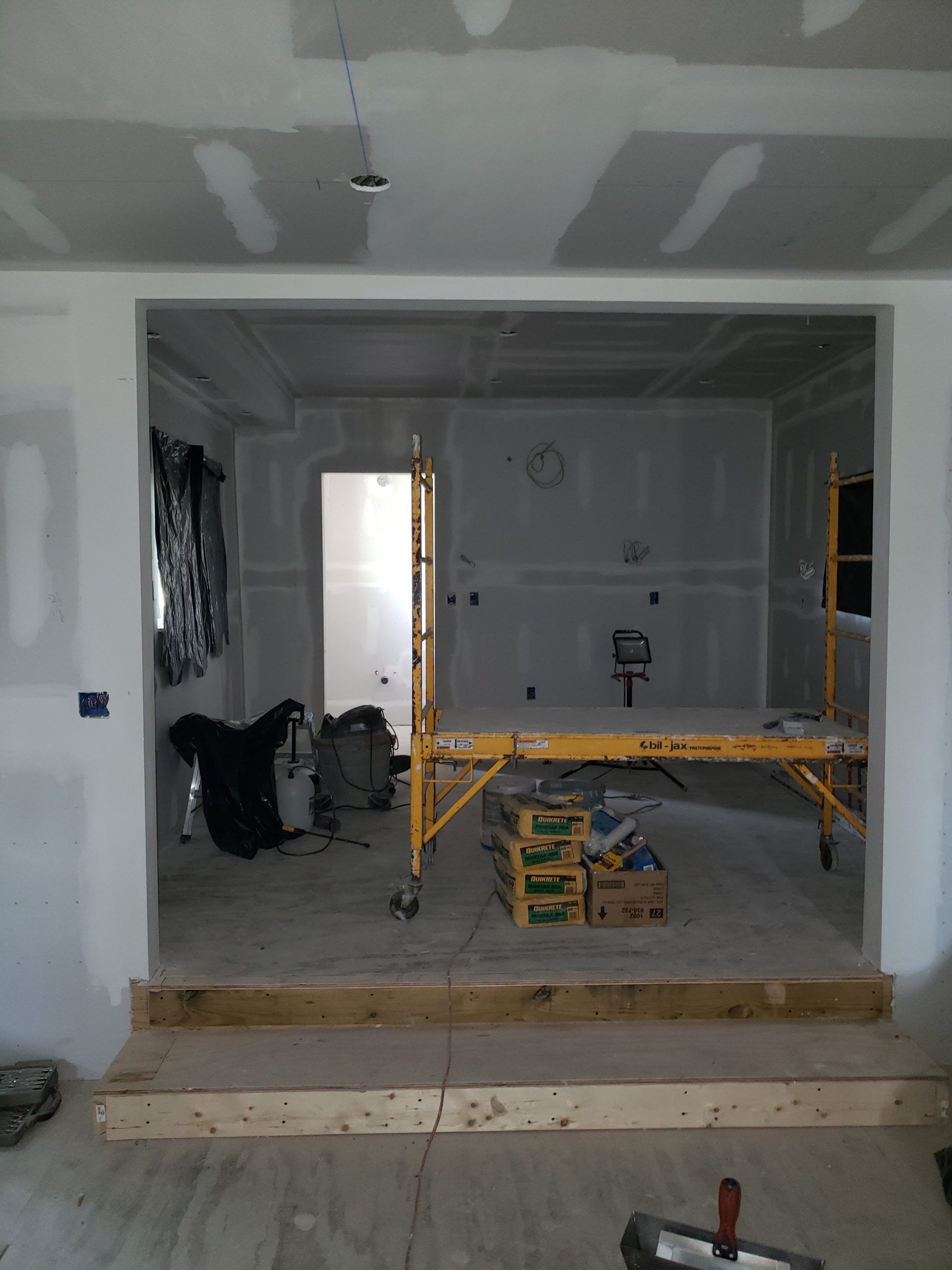 Interior of a room under construction with drywall and a scaffolding setup. Light gray walls.