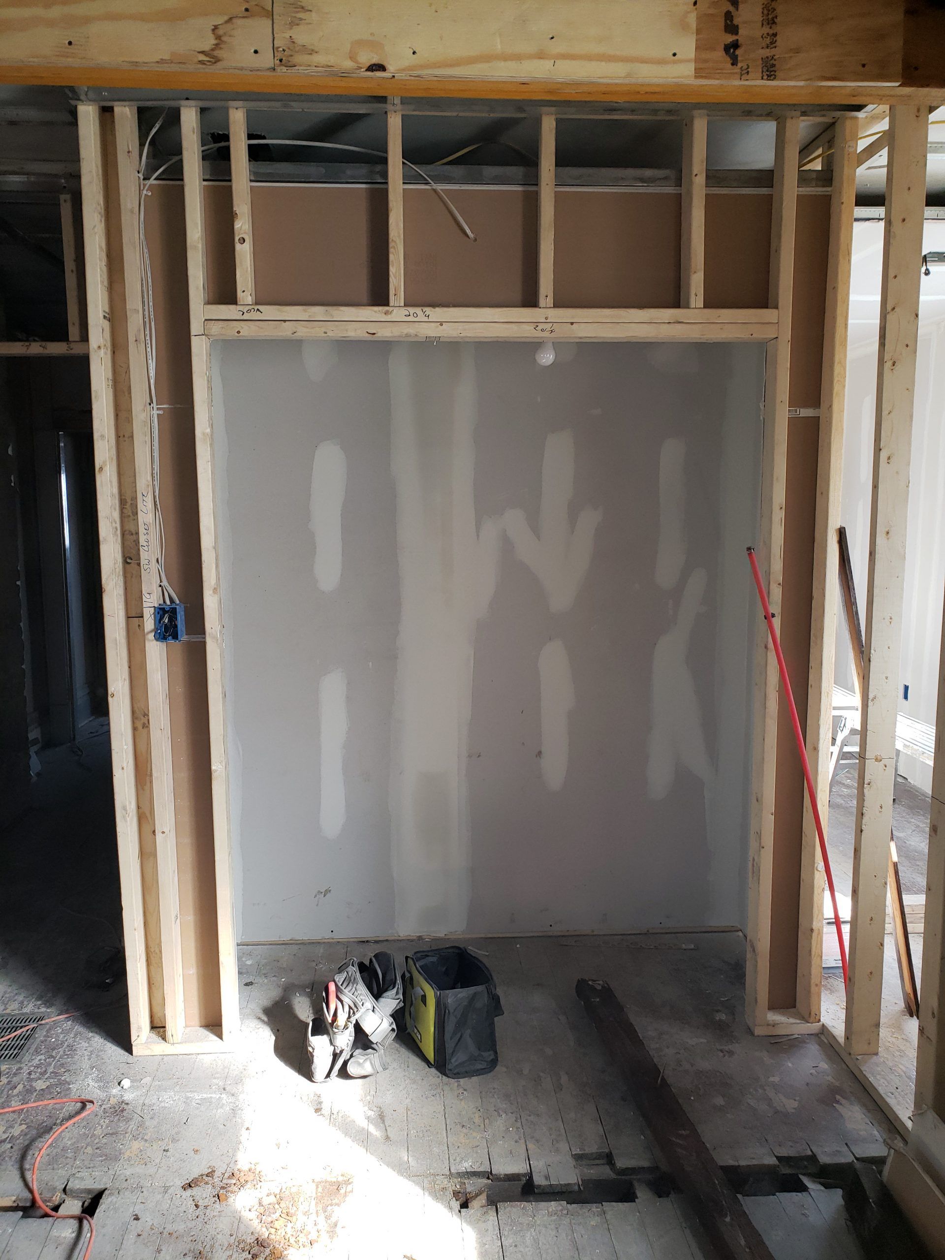 Interior construction: partially framed wall with drywall installed.  Tools and debris on the floor.