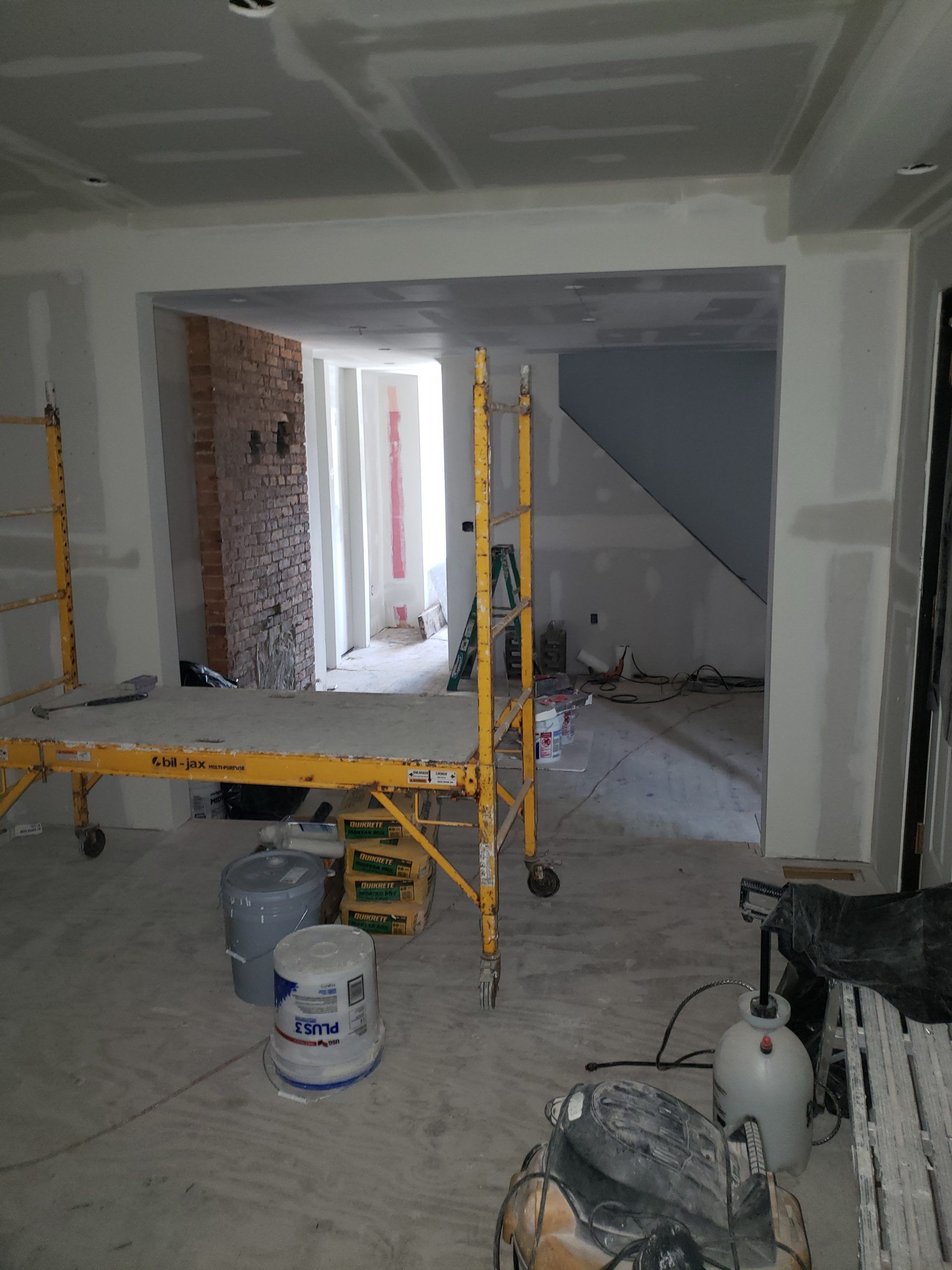 Interior construction in progress, yellow scaffolding, drywall, exposed brick, unfinished walls, various tools and materials.