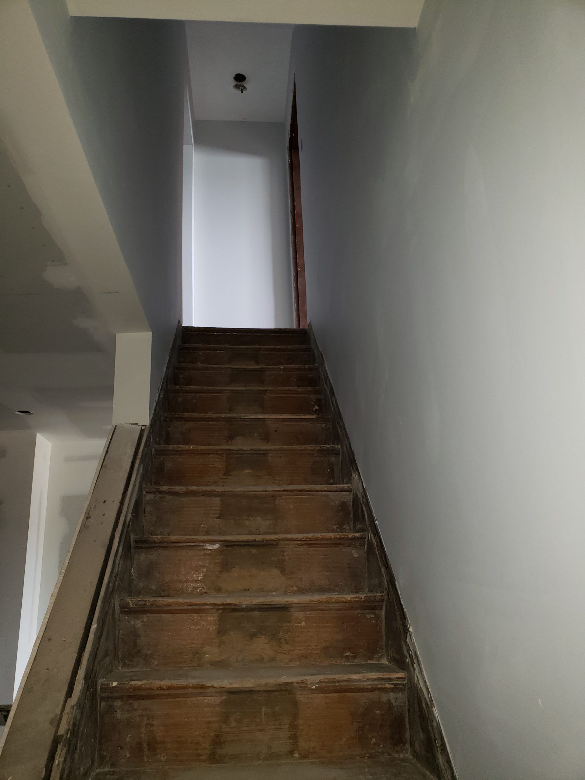 Wooden staircase with weathered steps, ascending to a white doorway. Walls painted gray and blue.
