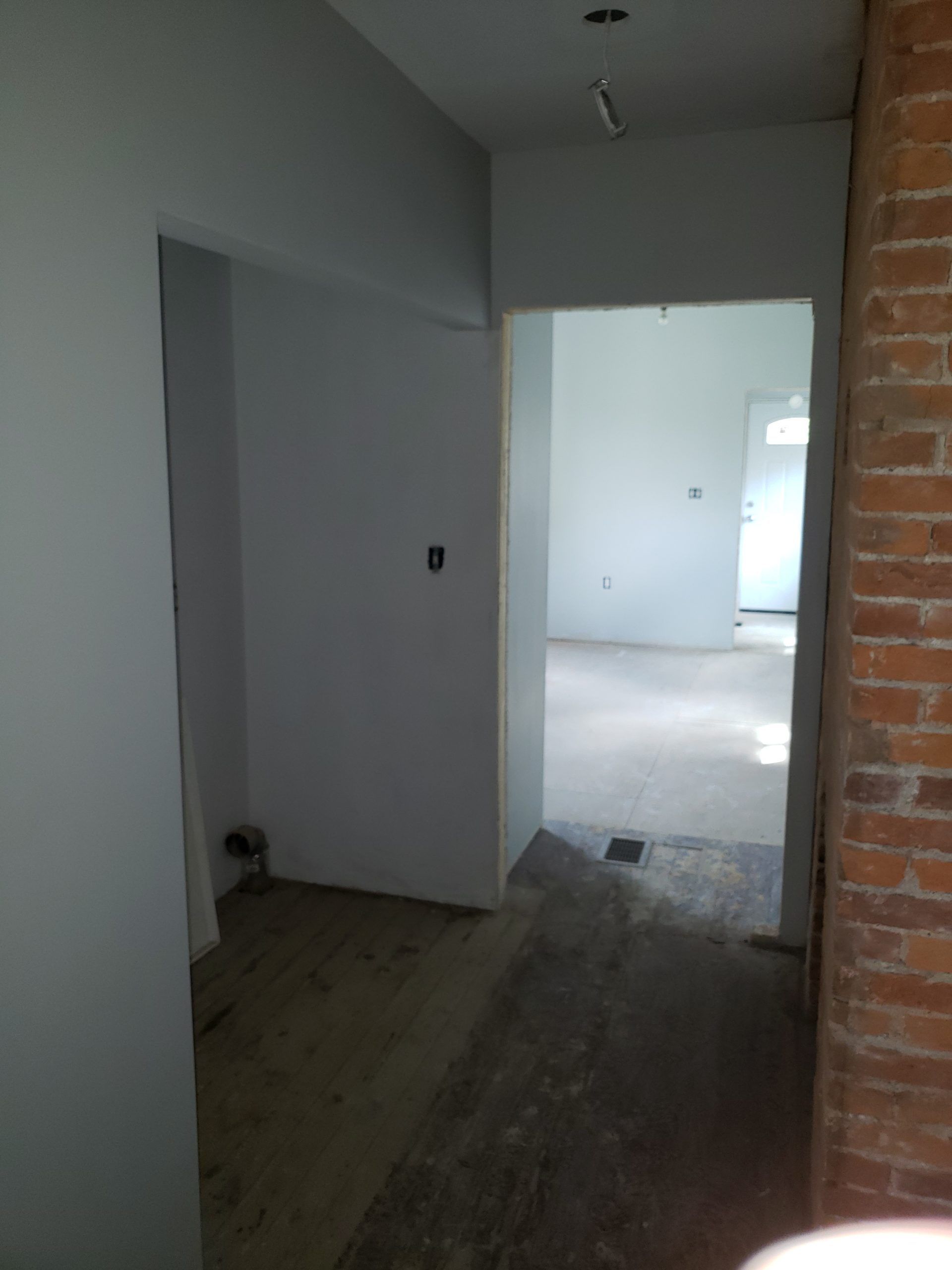 Hallway with open doorways, exposed brick wall on right, light-colored walls.