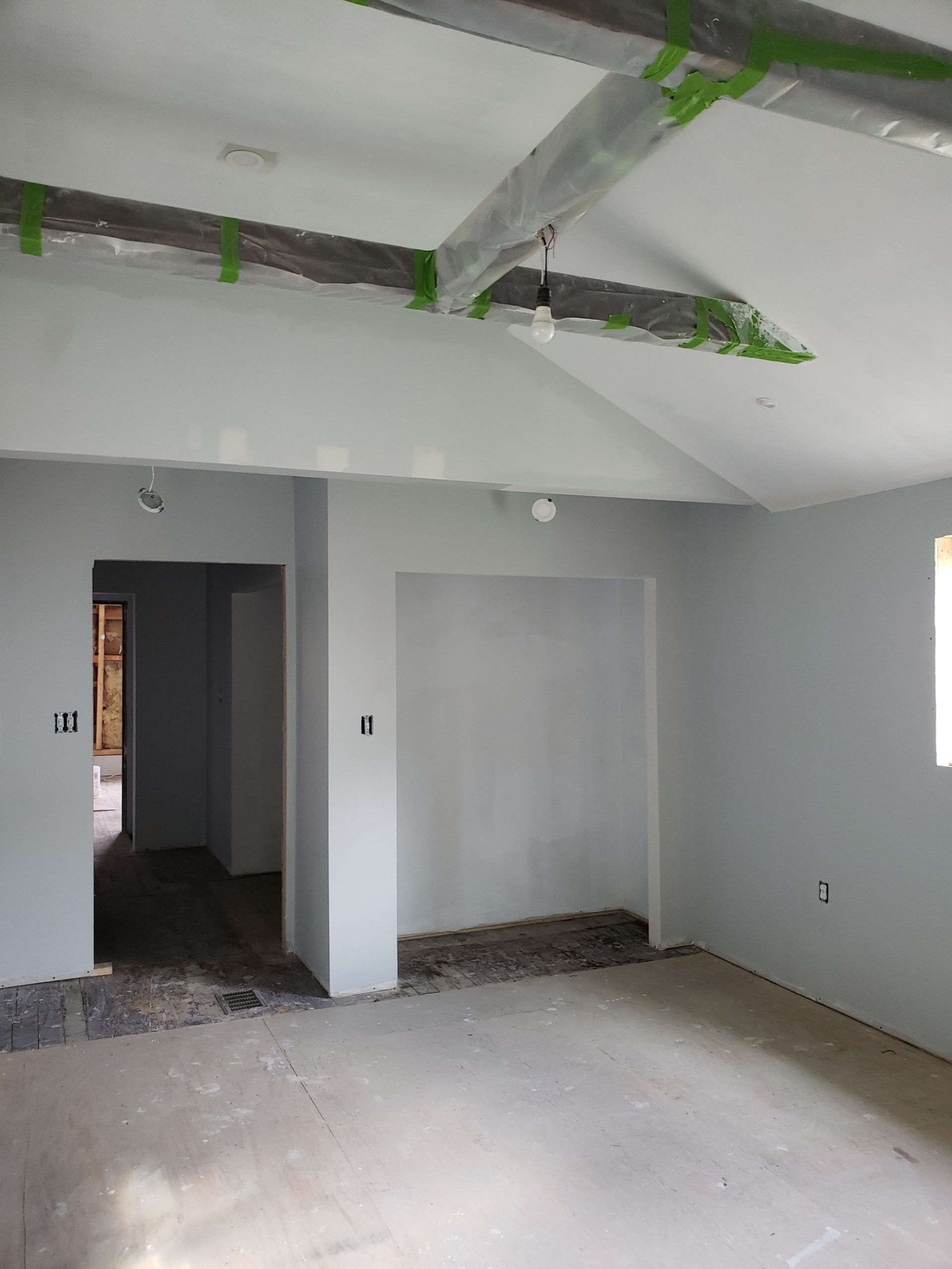 Interior of a room under construction, with gray walls, exposed ceiling beams, and concrete floor.
