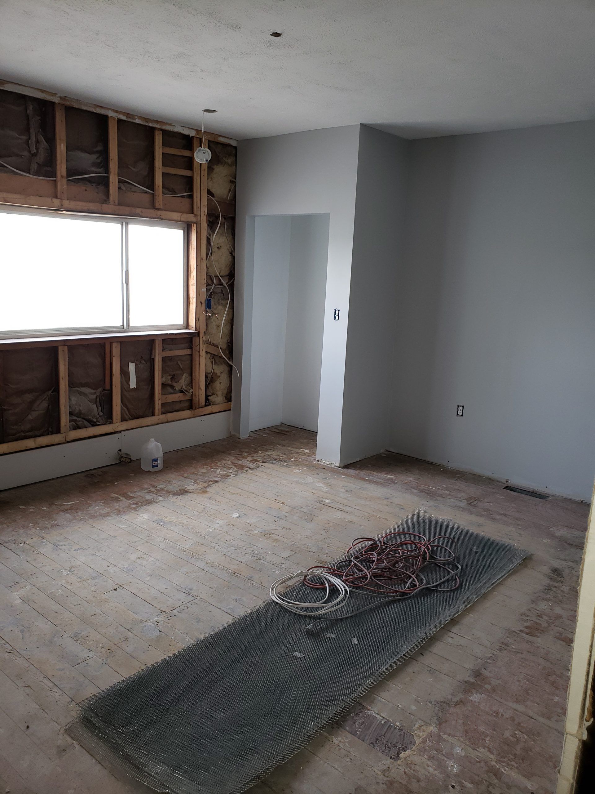 Room under renovation with exposed wall studs, window, and new gray paint.