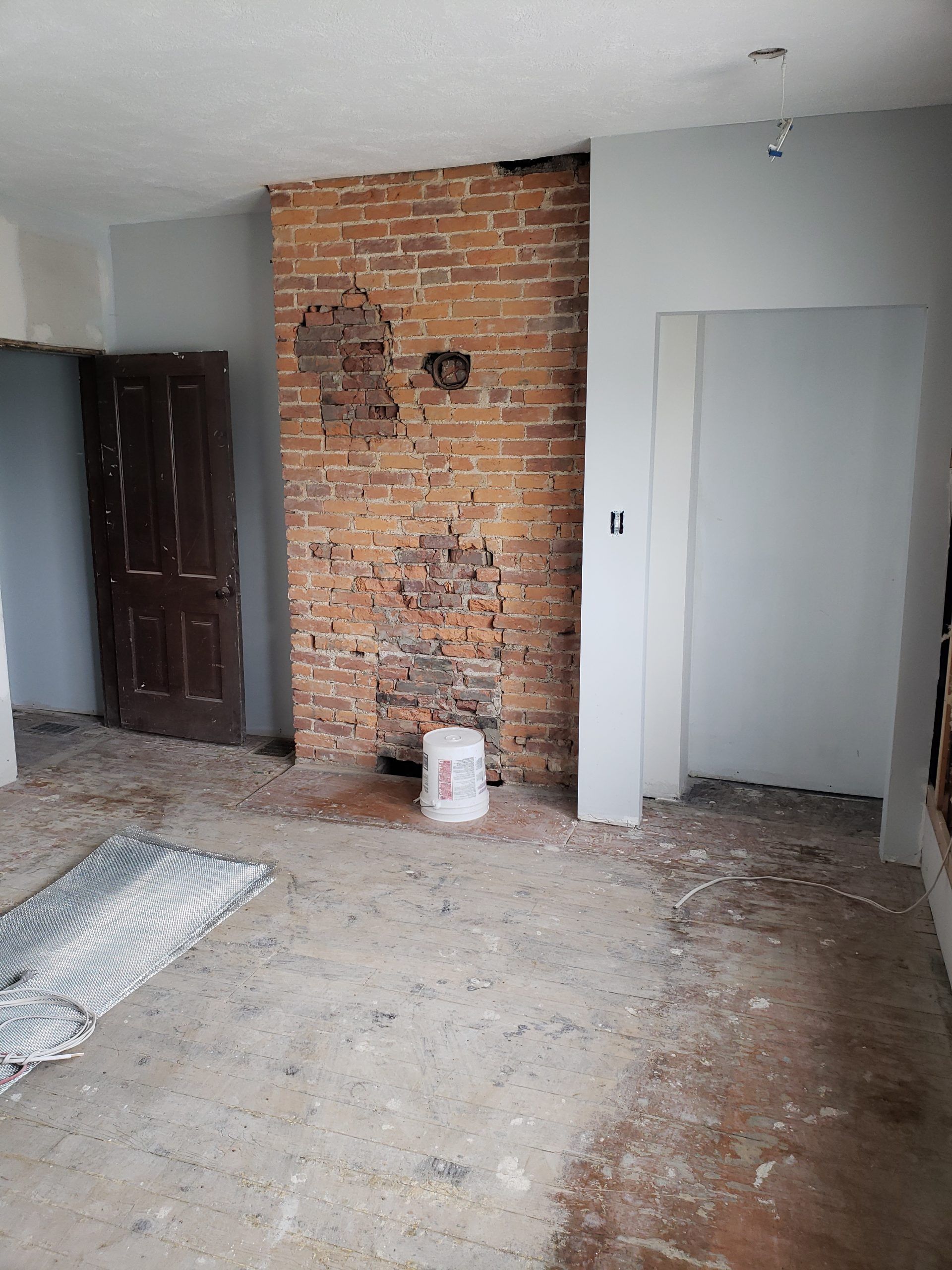Interior room under renovation, exposed brick chimney, unfinished walls and floor.