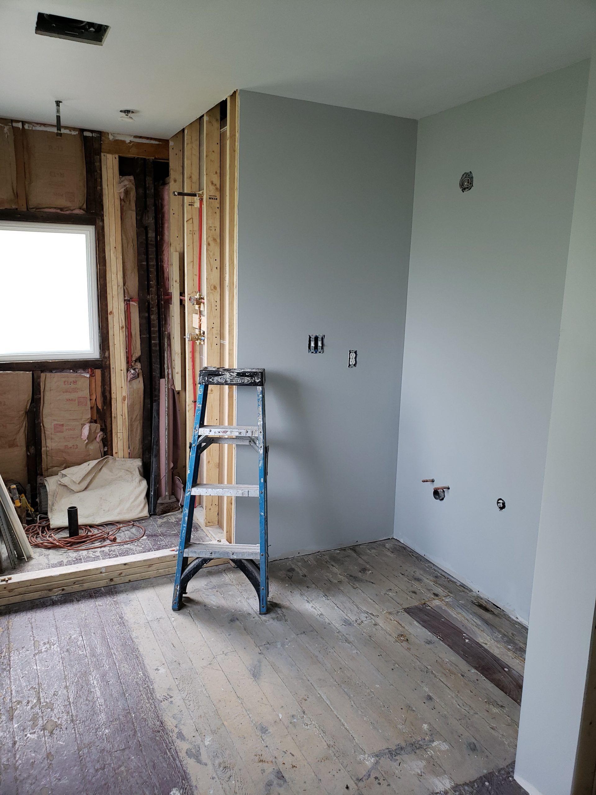 Interior construction site with ladder, exposed framing, and partially painted walls.