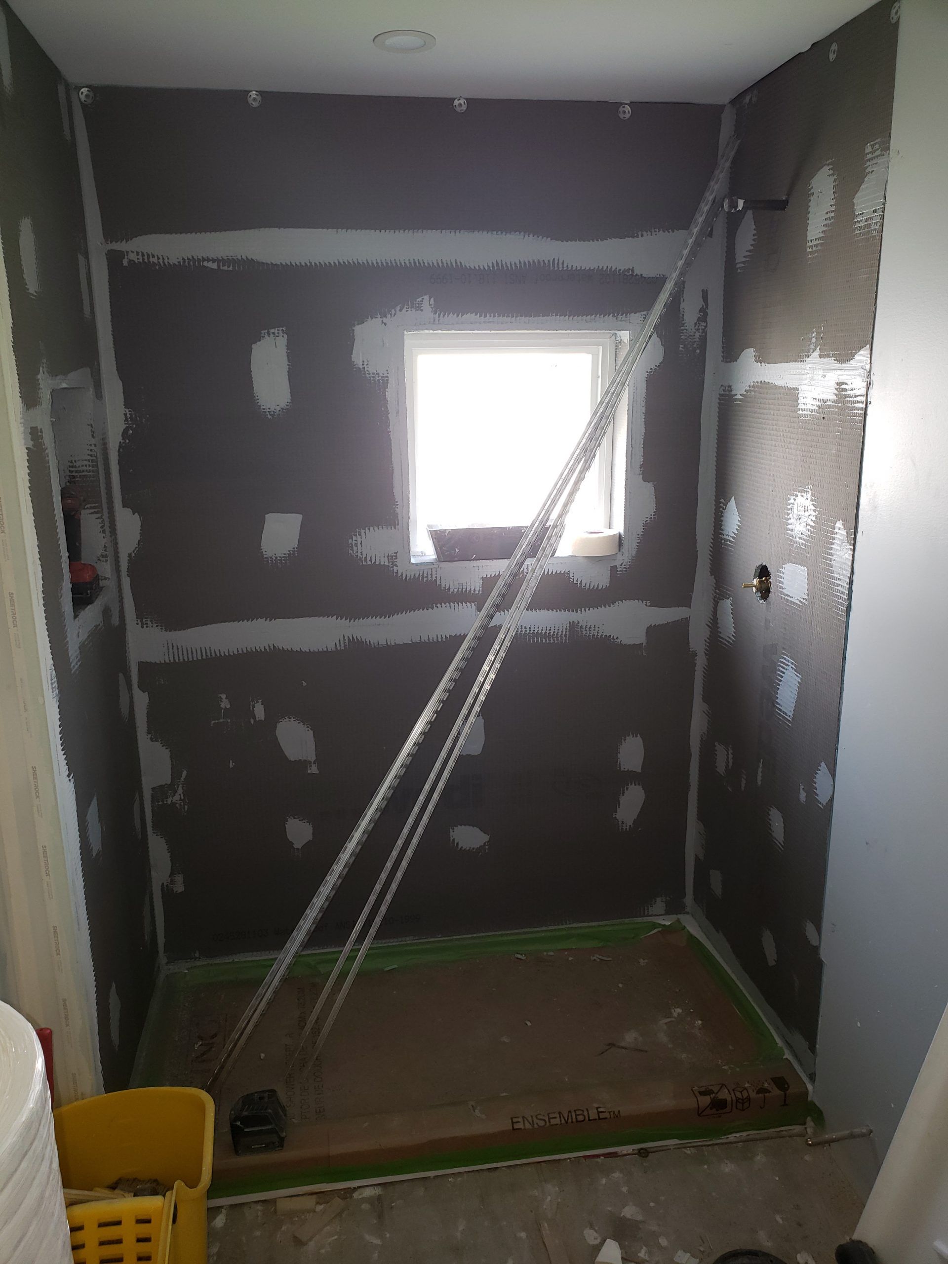 Bathroom under construction; dark gray walls, small window, shower base. Chains suspended.