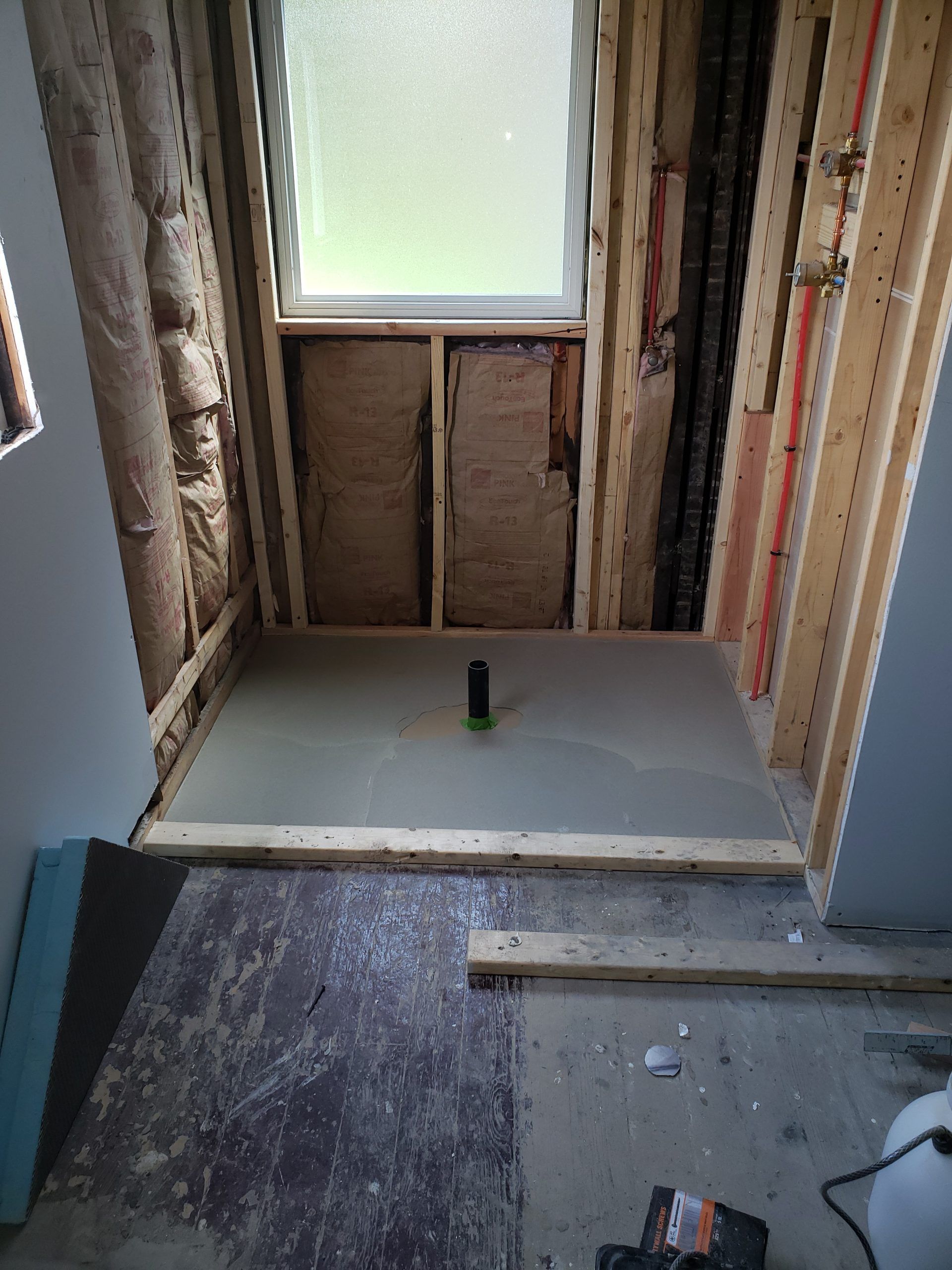Bathroom under construction: shower base, window, exposed framing, insulation.