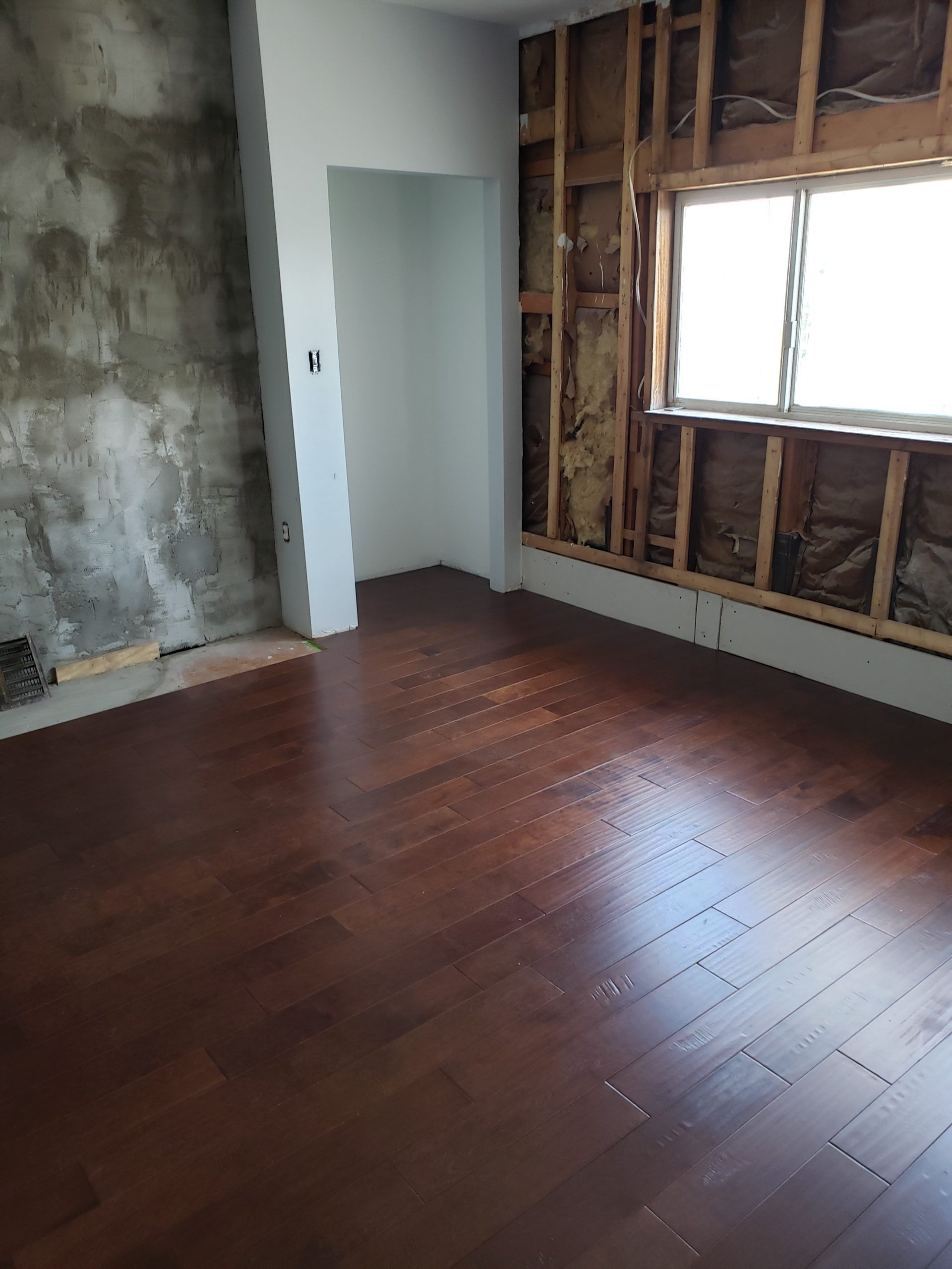 Room under construction with herringbone wood floor, exposed wall studs, window, and partially finished concrete wall.