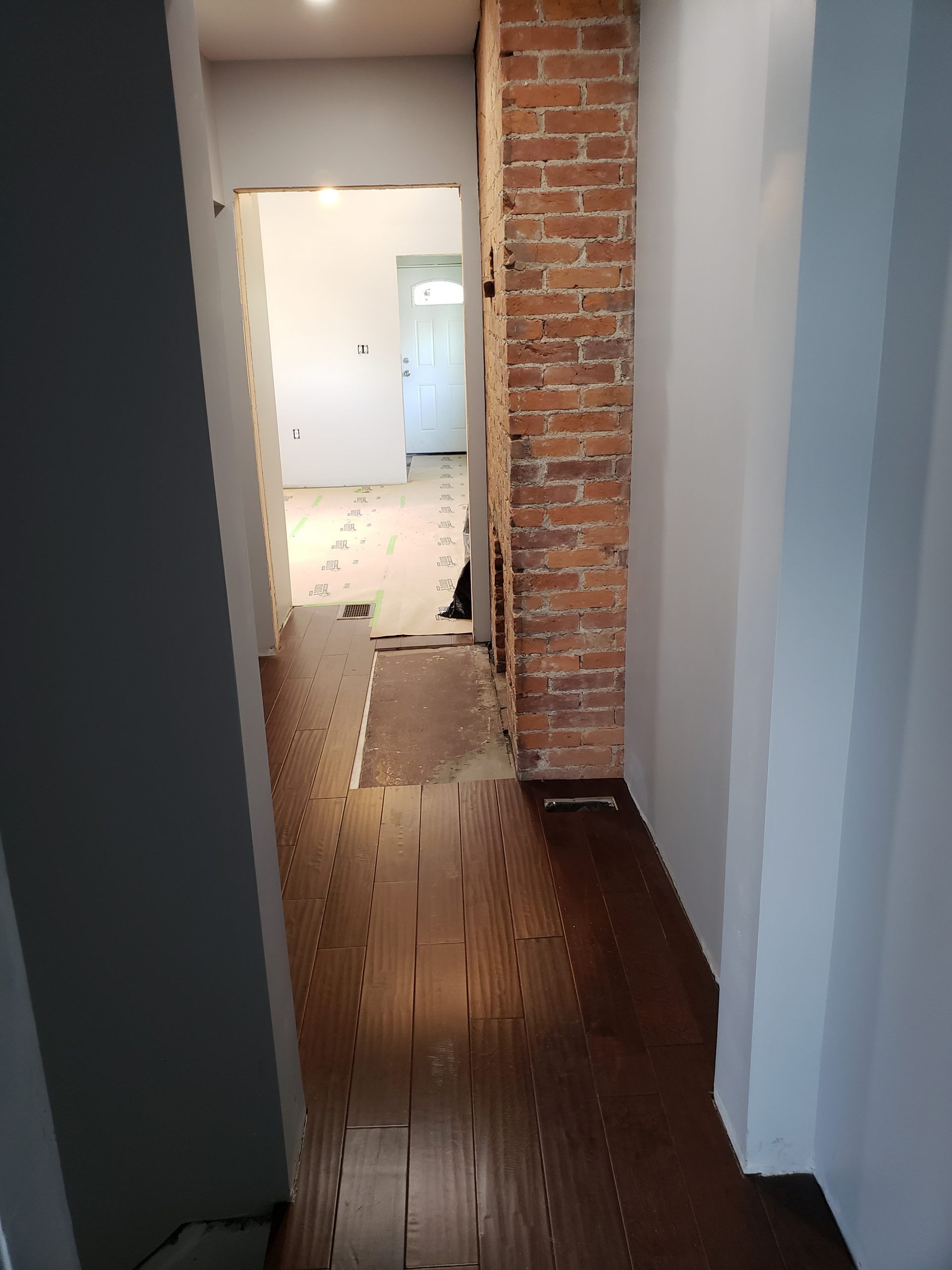 Hallway renovation with exposed brick chimney and partially installed dark wood flooring.
