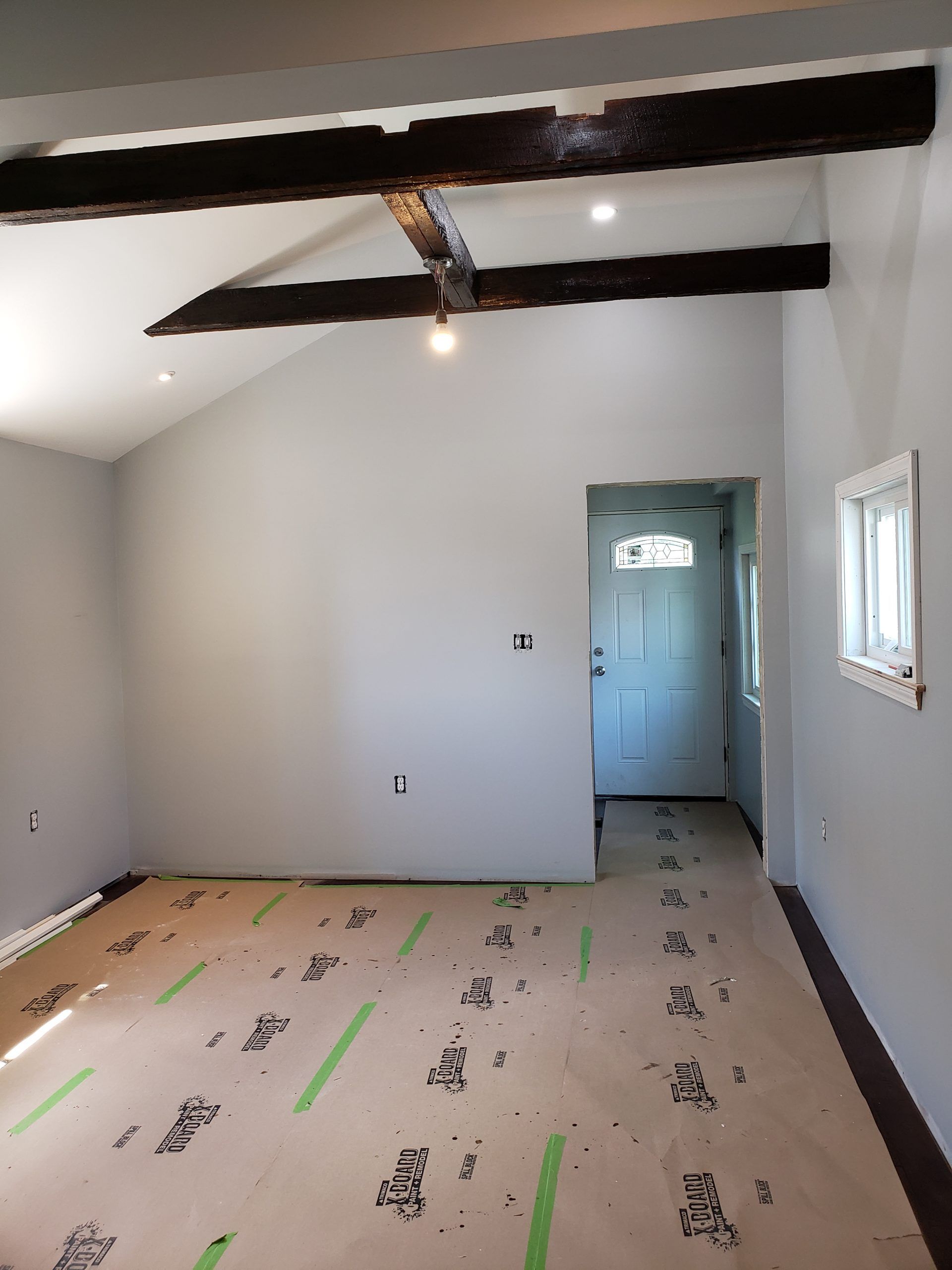 Interior of a room with exposed wooden beams, gray walls, and a white door at the end.