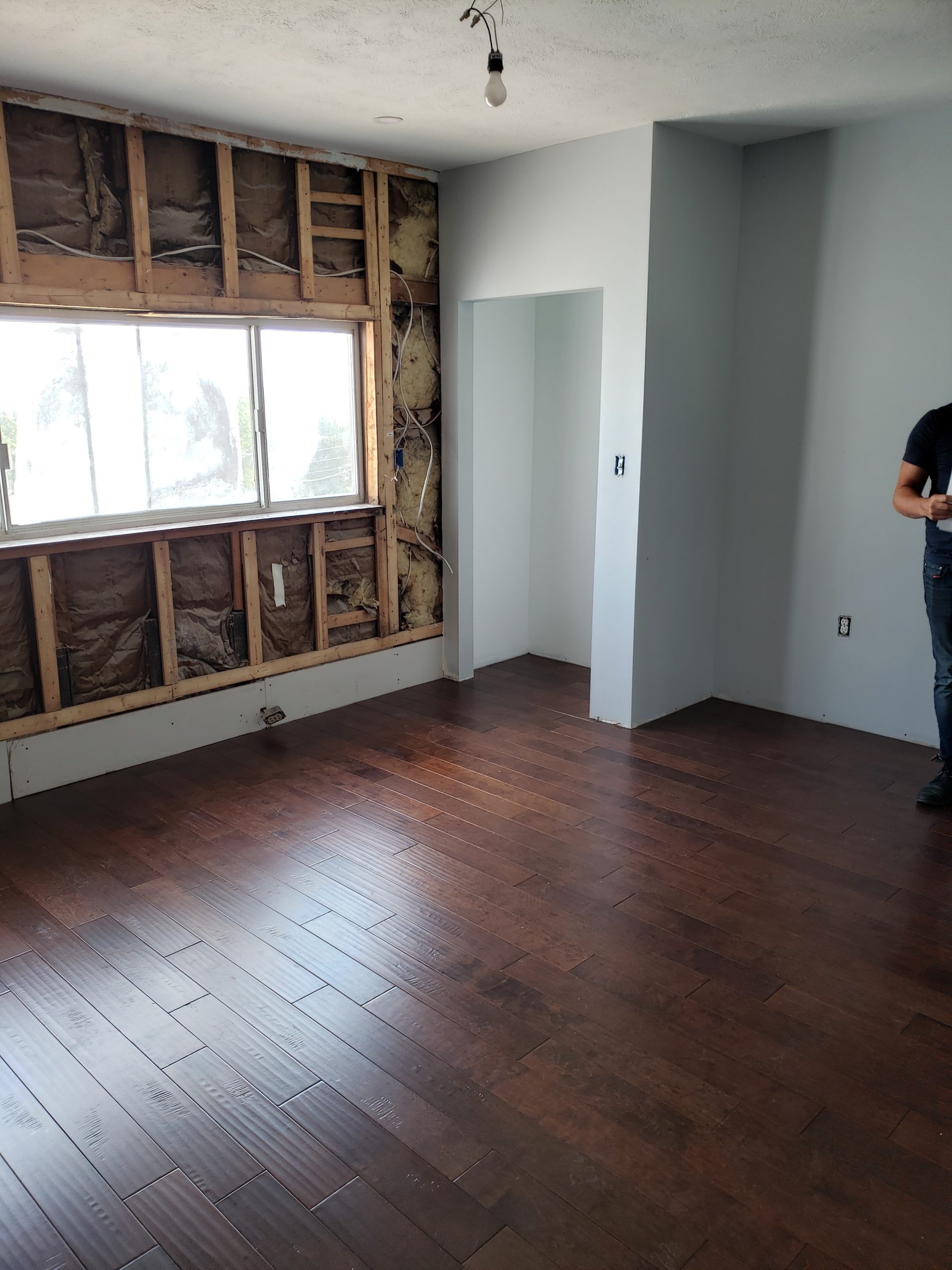 Room under renovation with exposed wall studs, dark wood floor, and doorway.