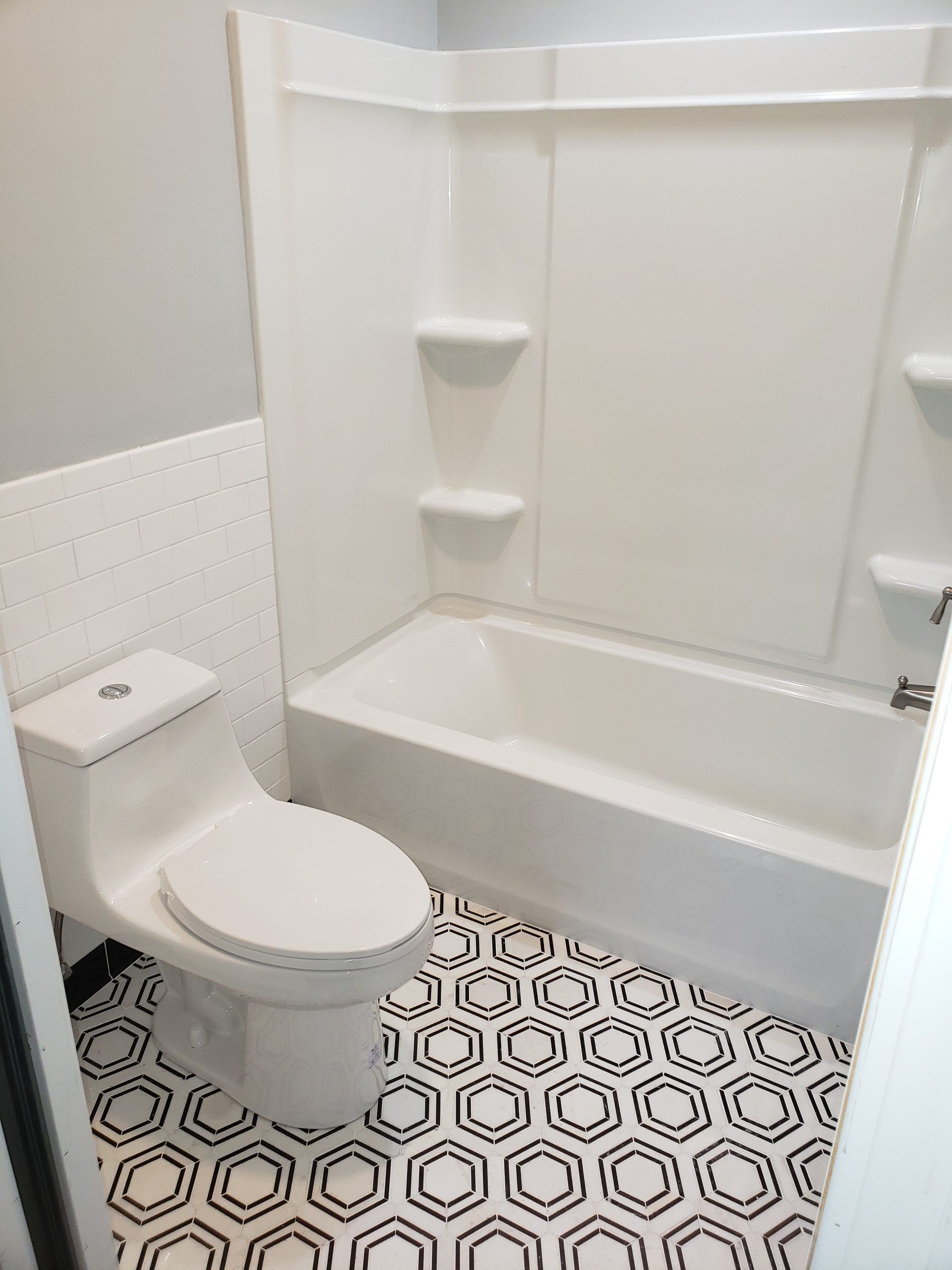 White bathroom with a tub, toilet, and black and white hexagon tile floor.