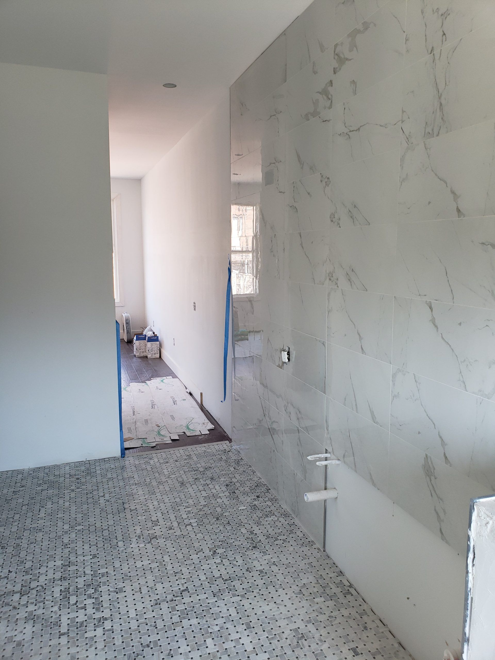 Bathroom under construction; white marble shower wall, patterned floor tile, hallway.