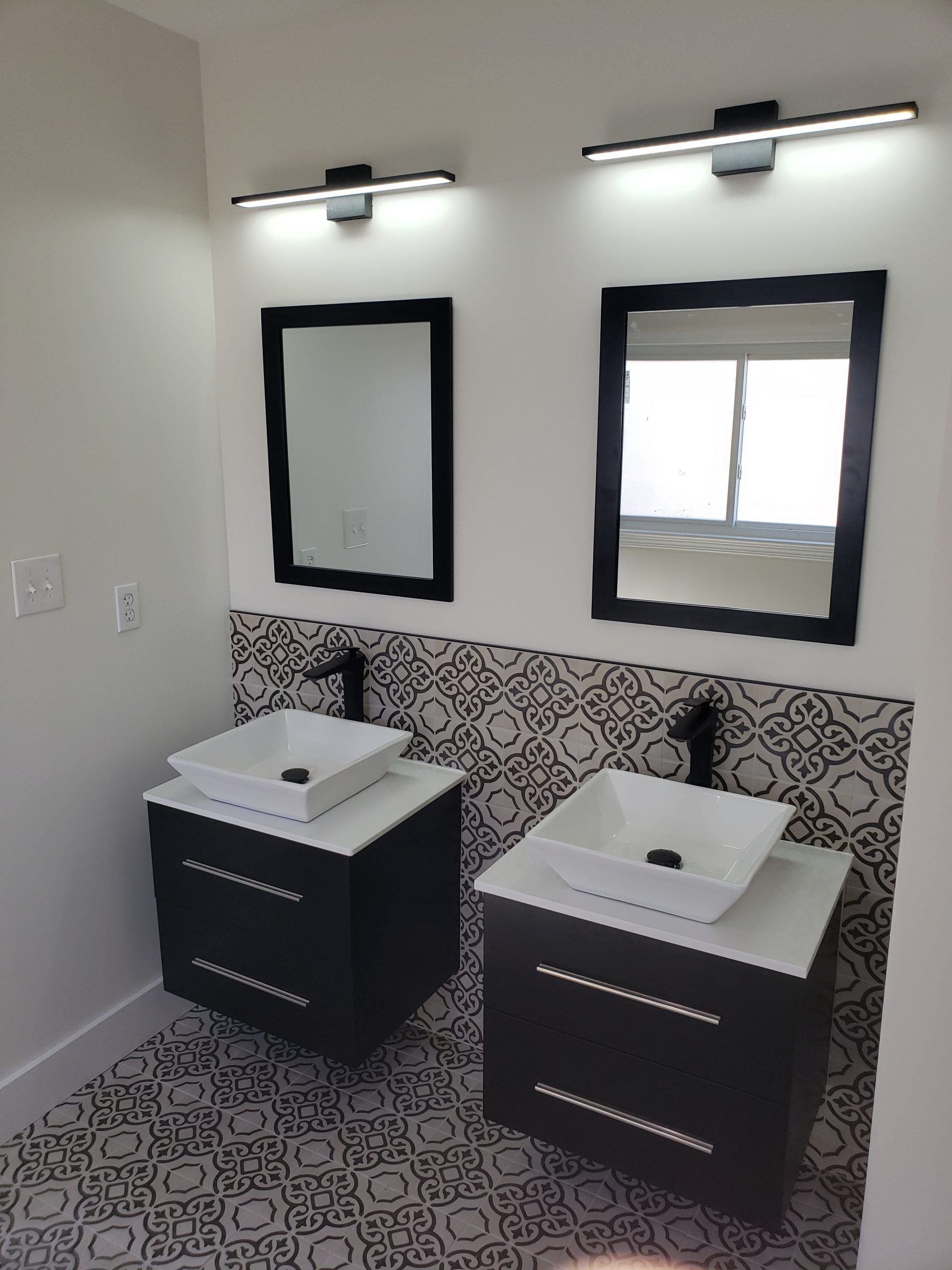 Two modern bathroom vanities with black accents, each with a mirror and overhead light.