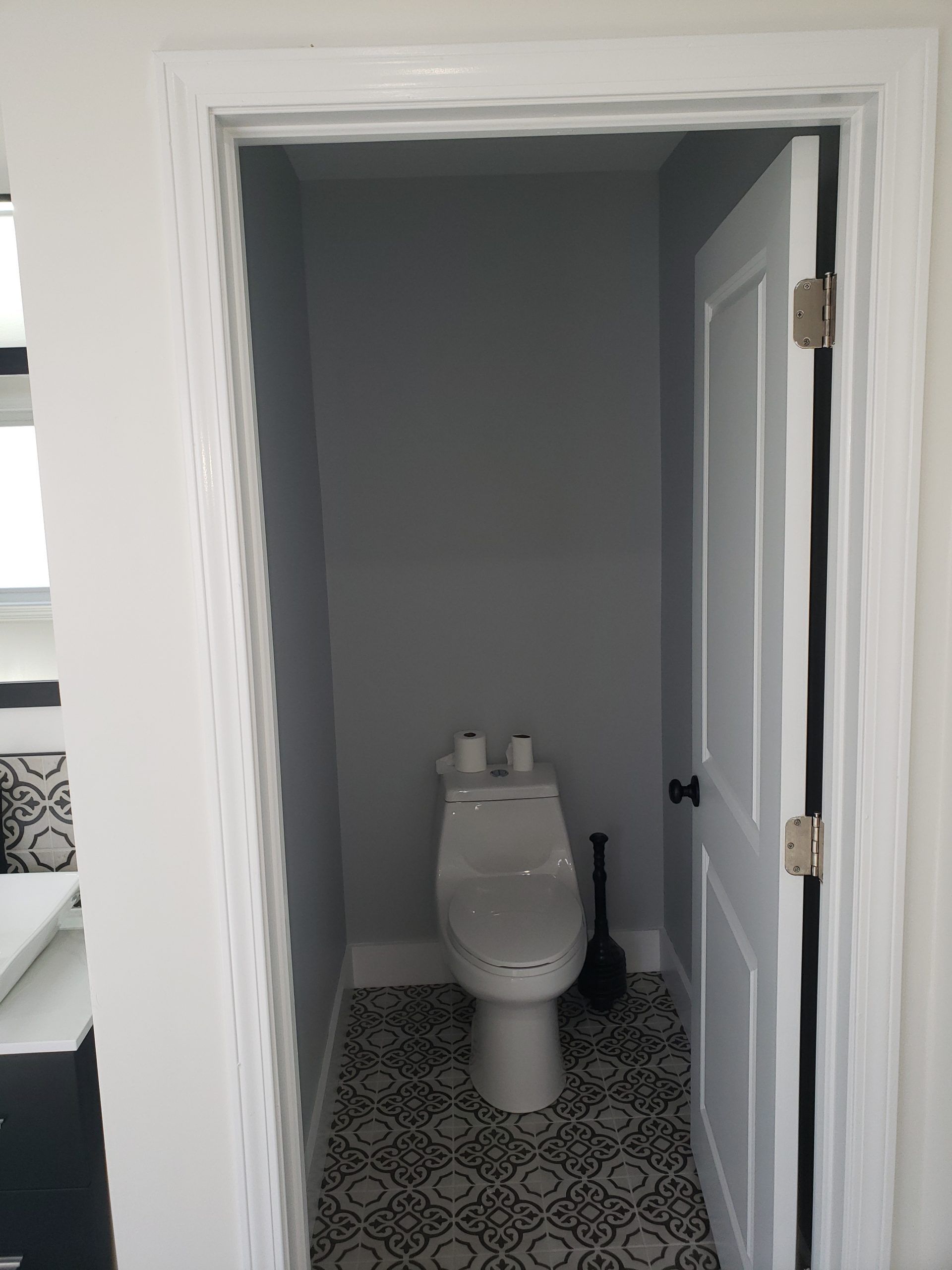 Bathroom with gray walls, white door, patterned floor, and a white toilet.