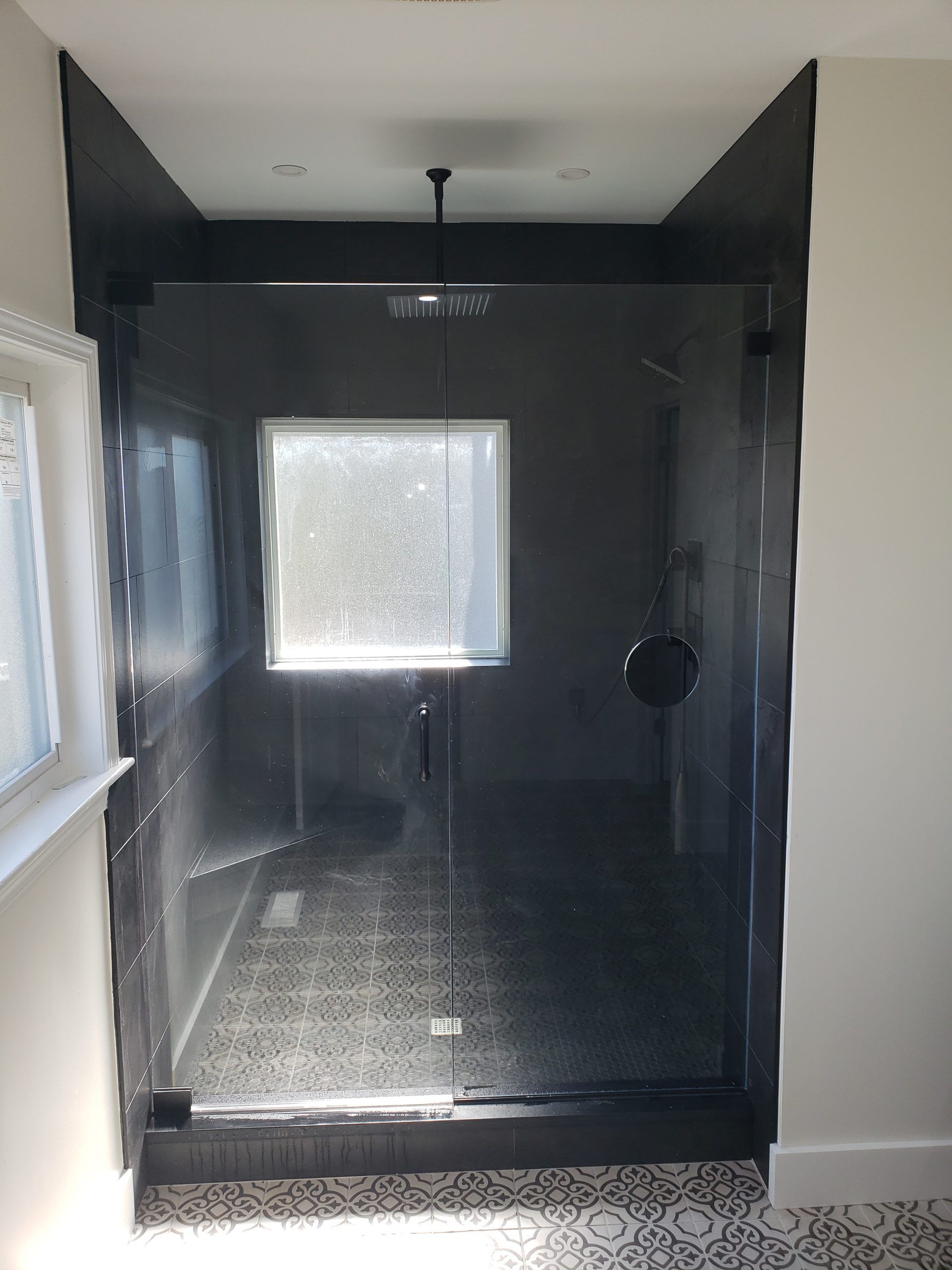 Bathroom with a glass shower enclosure and a rain showerhead. Black trim, patterned floor.