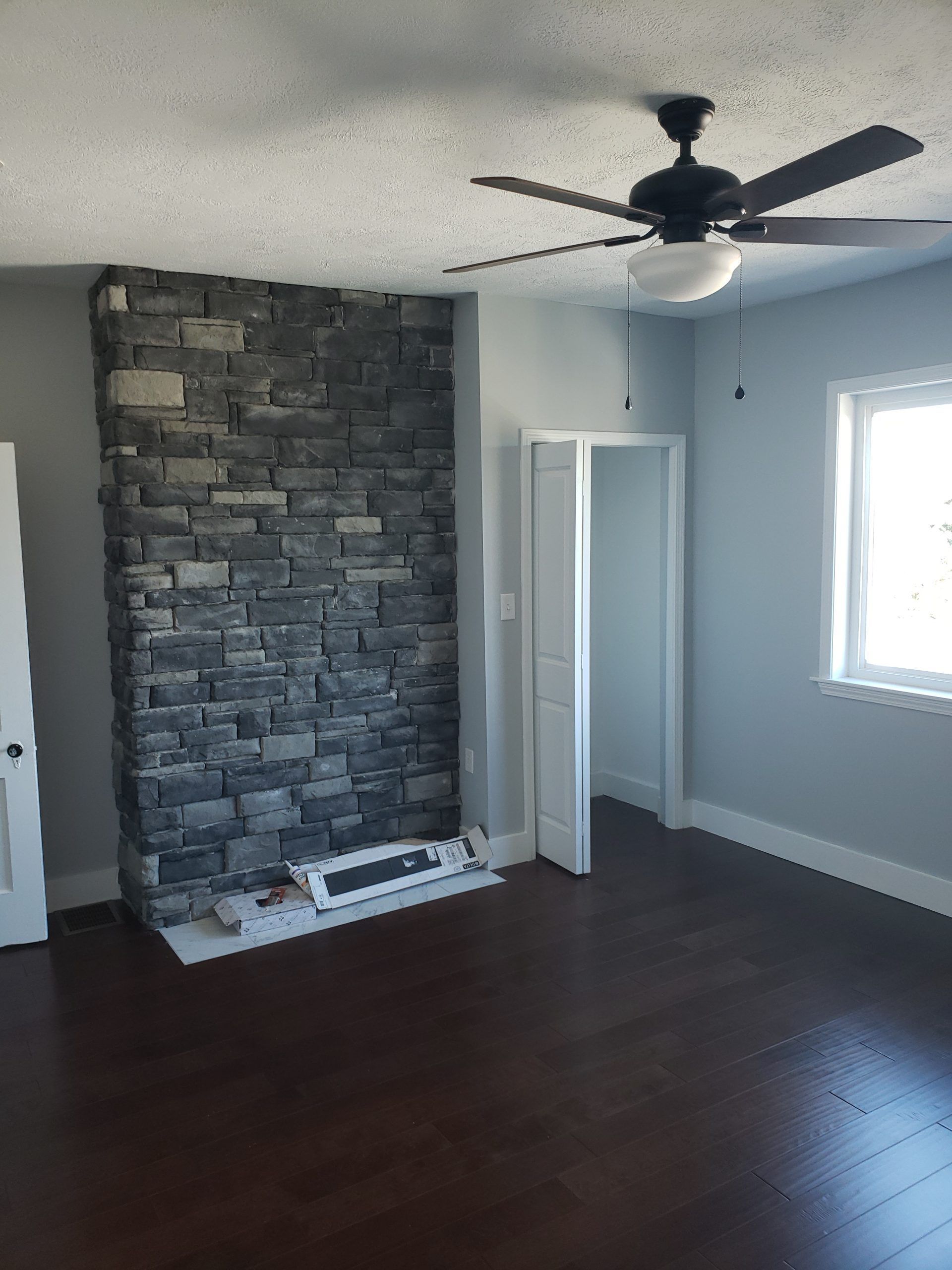 Living room with a stone fireplace, dark wood floor, and ceiling fan.