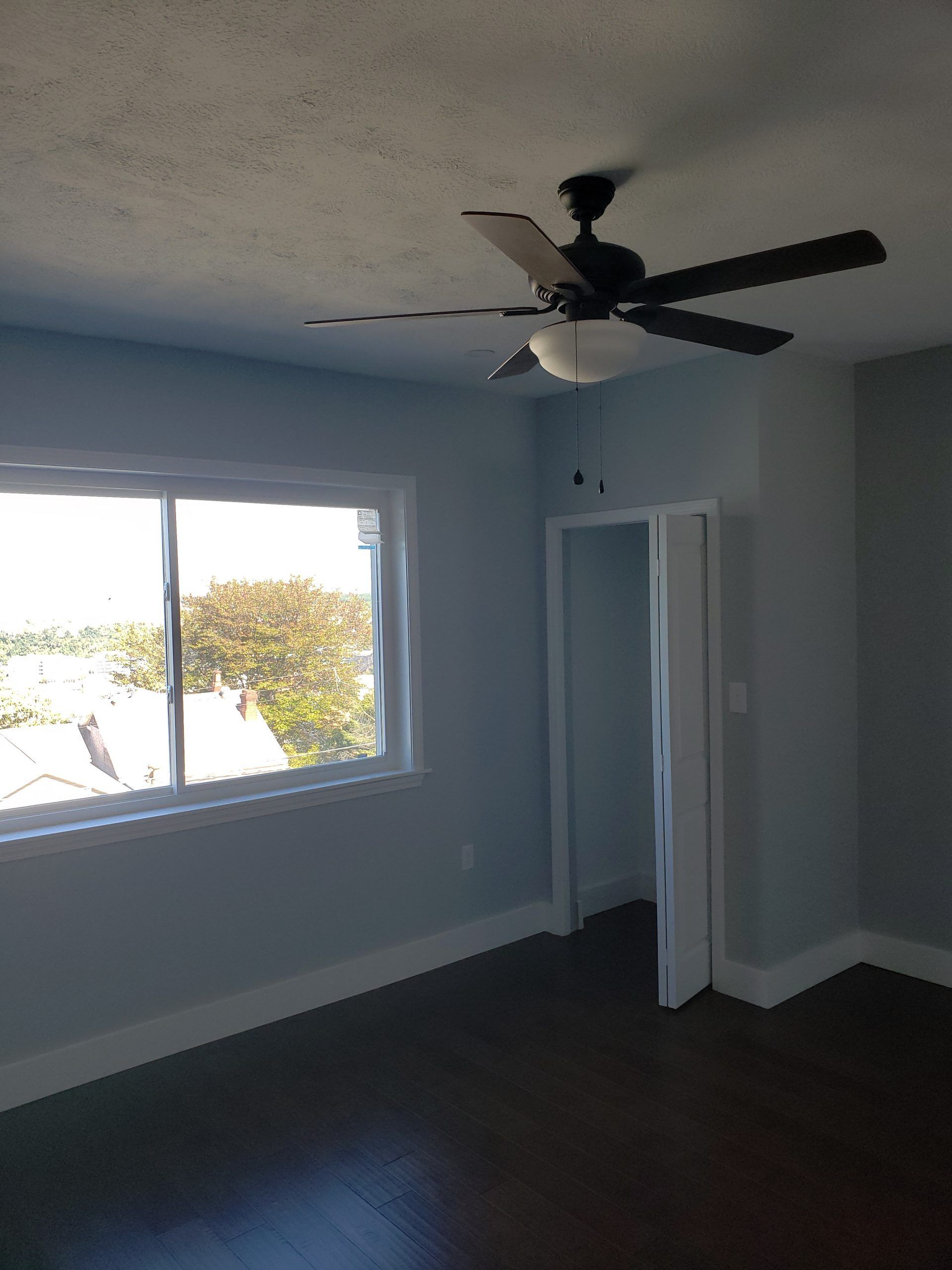 Bedroom with a window, ceiling fan, dark floors, and light blue walls.