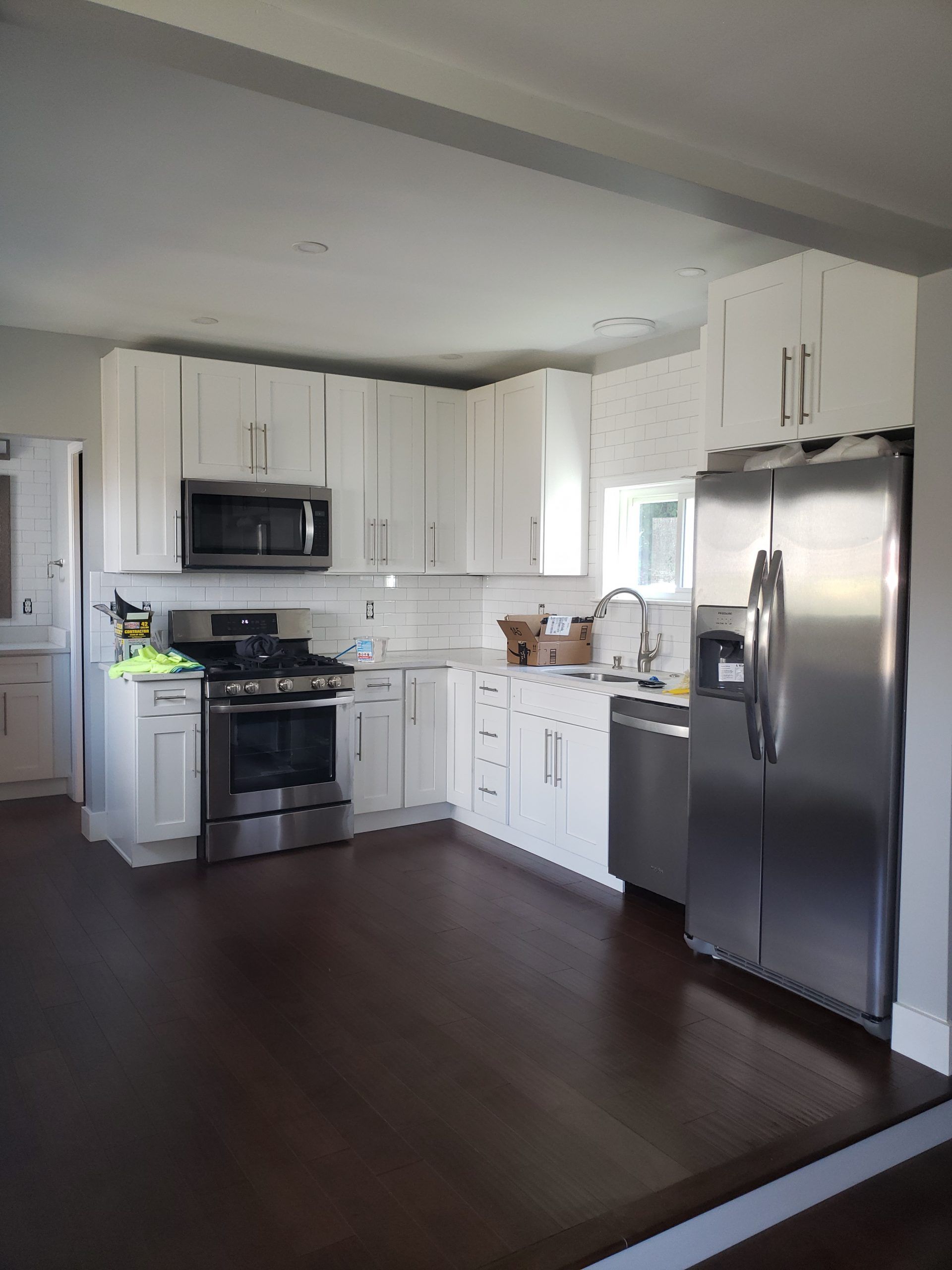 White kitchen with stainless steel appliances and dark wood floor.