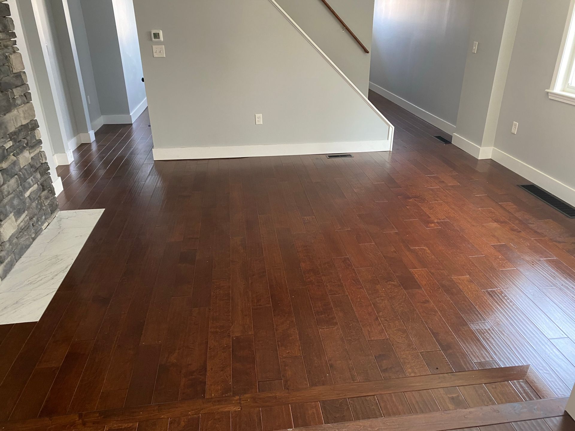 Dark hardwood floor in a home with gray walls, a staircase, and a stone fireplace.