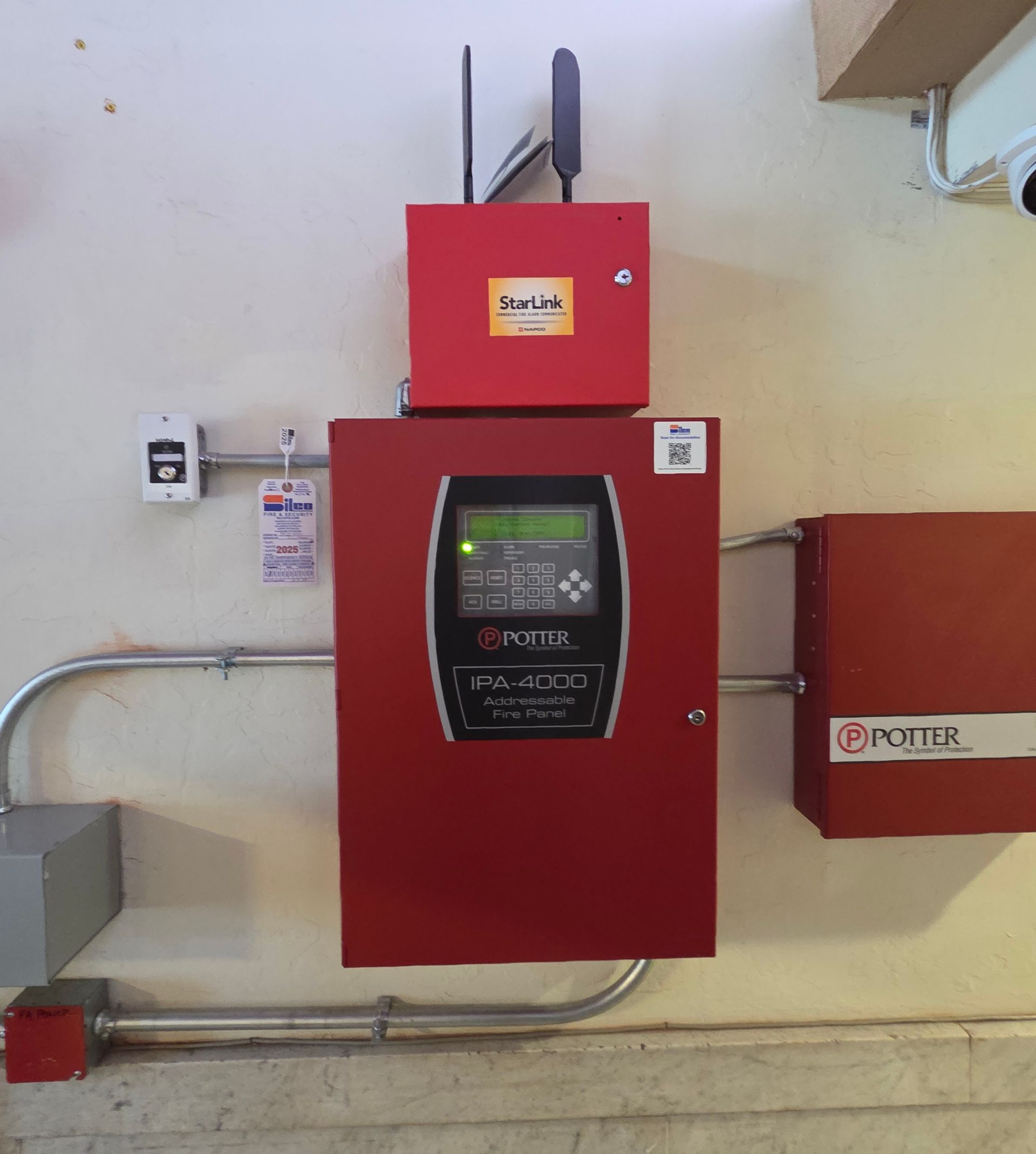 Red electrical control panel with display, mounted on a wall beside conduit and junction boxes.