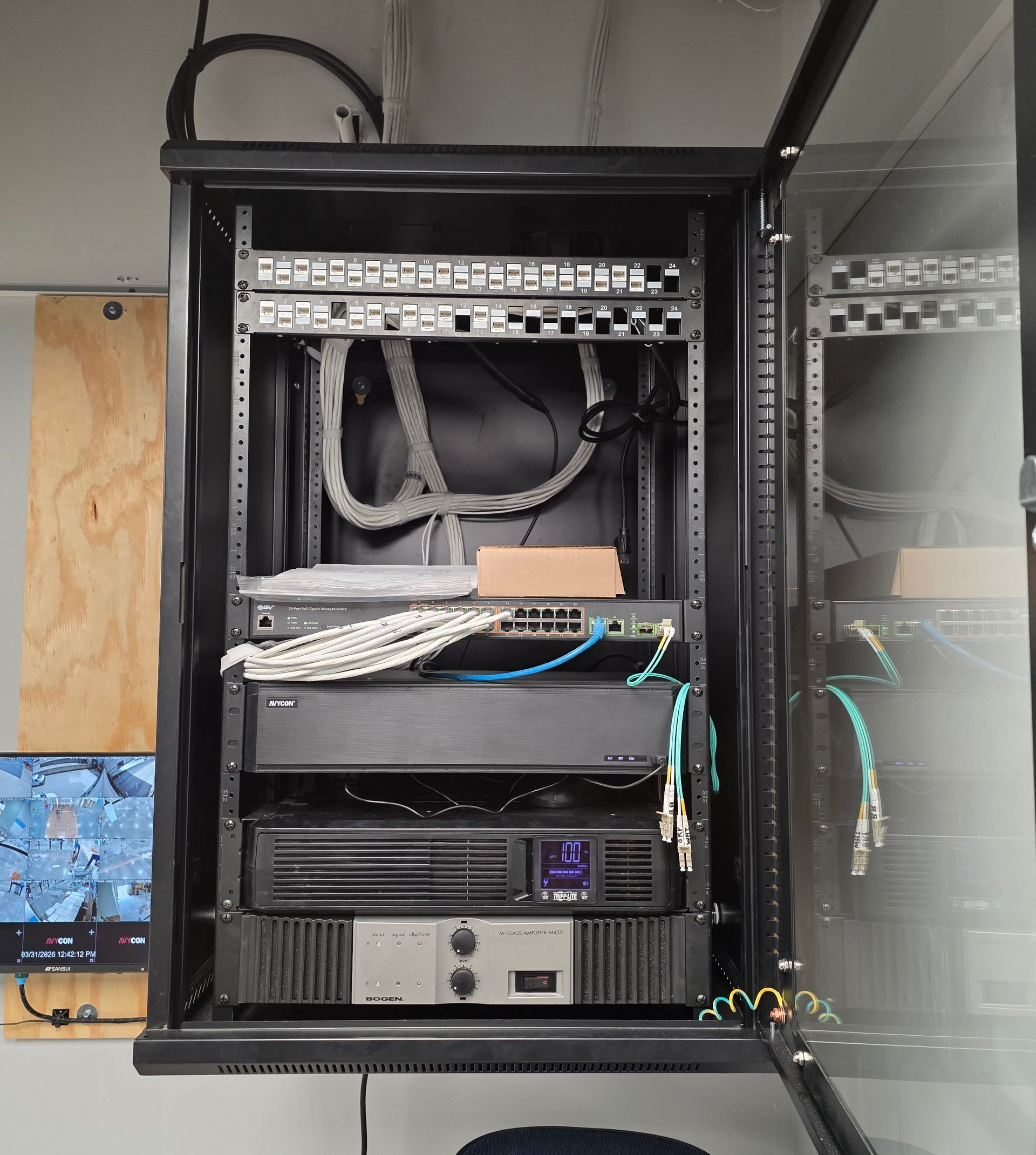 Open network server rack with patch panels, switches, and cables in a room with a glass wall