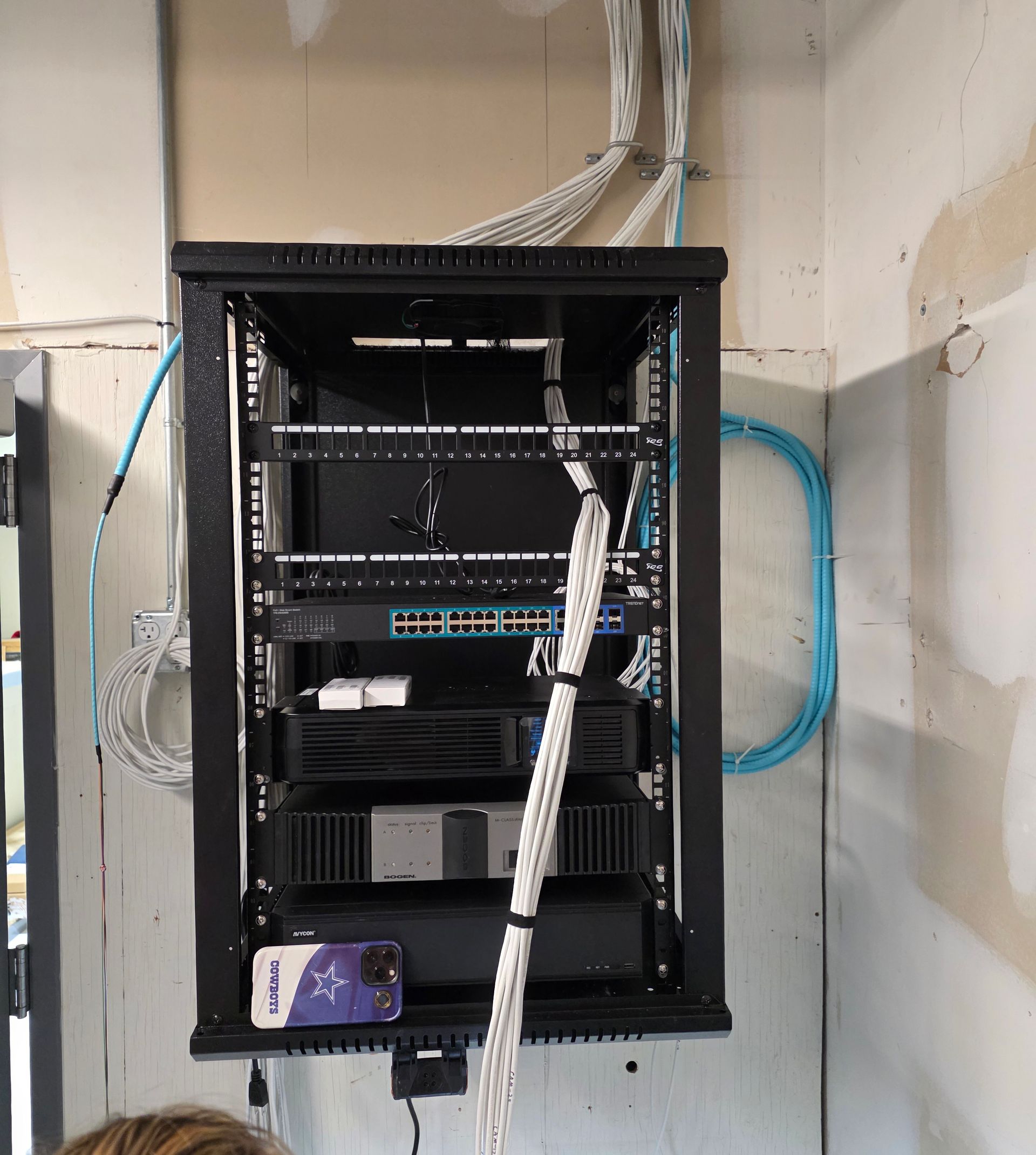 Wall-mounted network rack with routers, switches, and bundled cables in a utility room