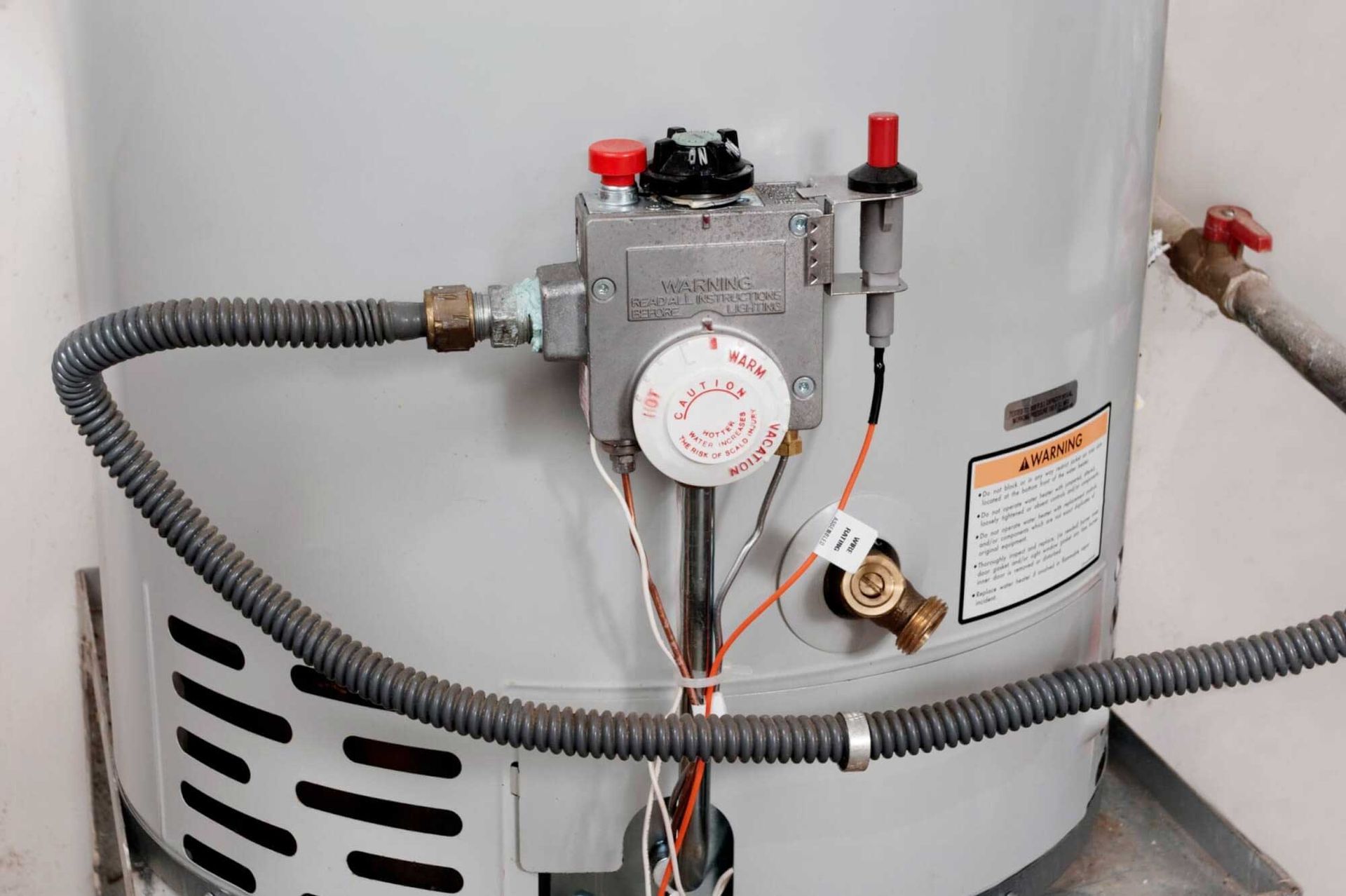 Water heater with control panel, gas line, and warning label.