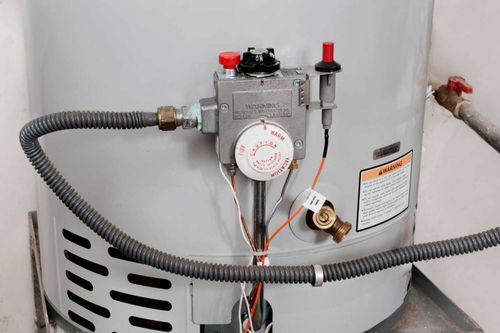 Water heater with control panel, gas line, and warning label.