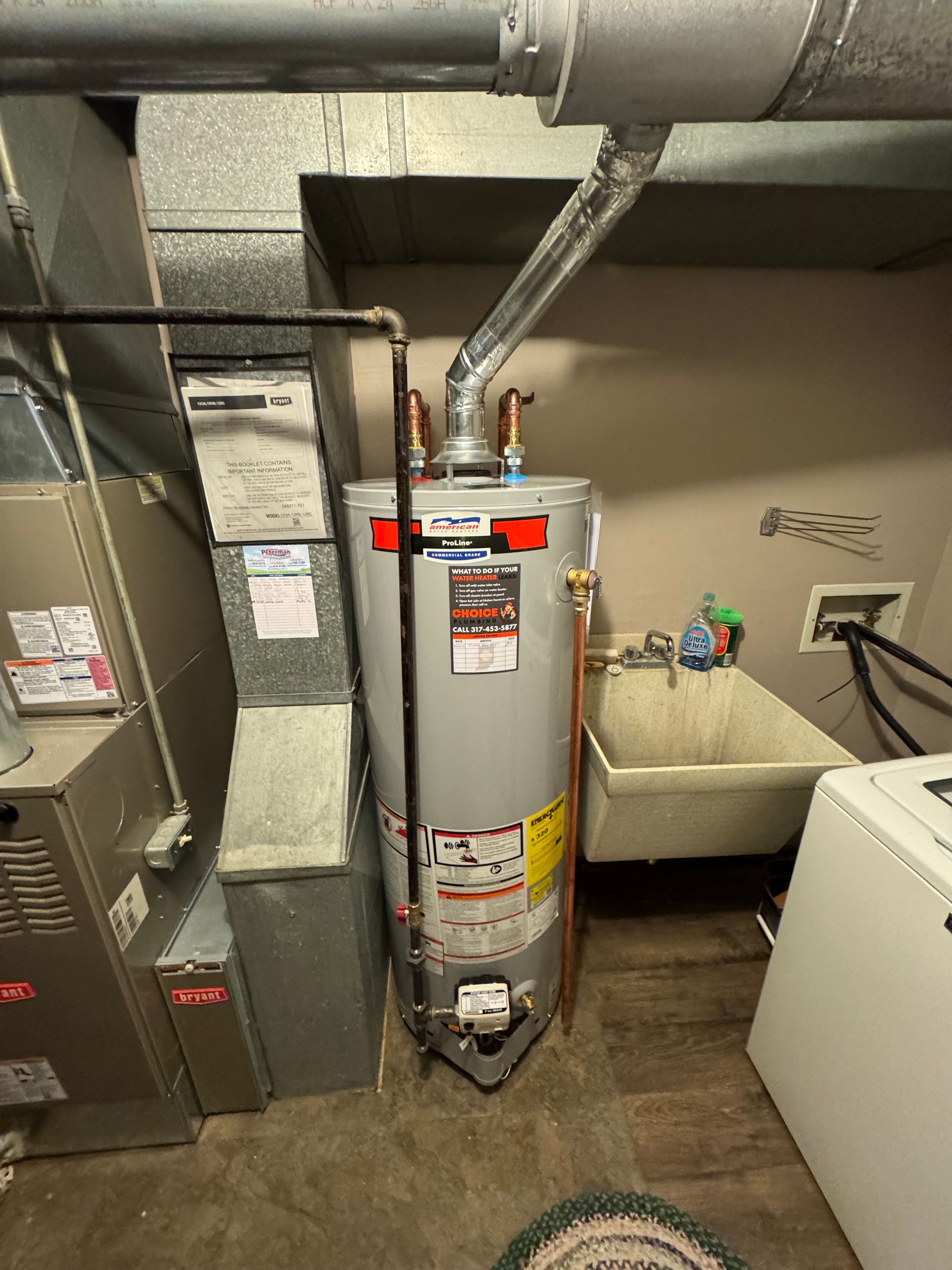 A grey water heater stands in a basement next to a metal furnace, a utility sink, and a washing machine.