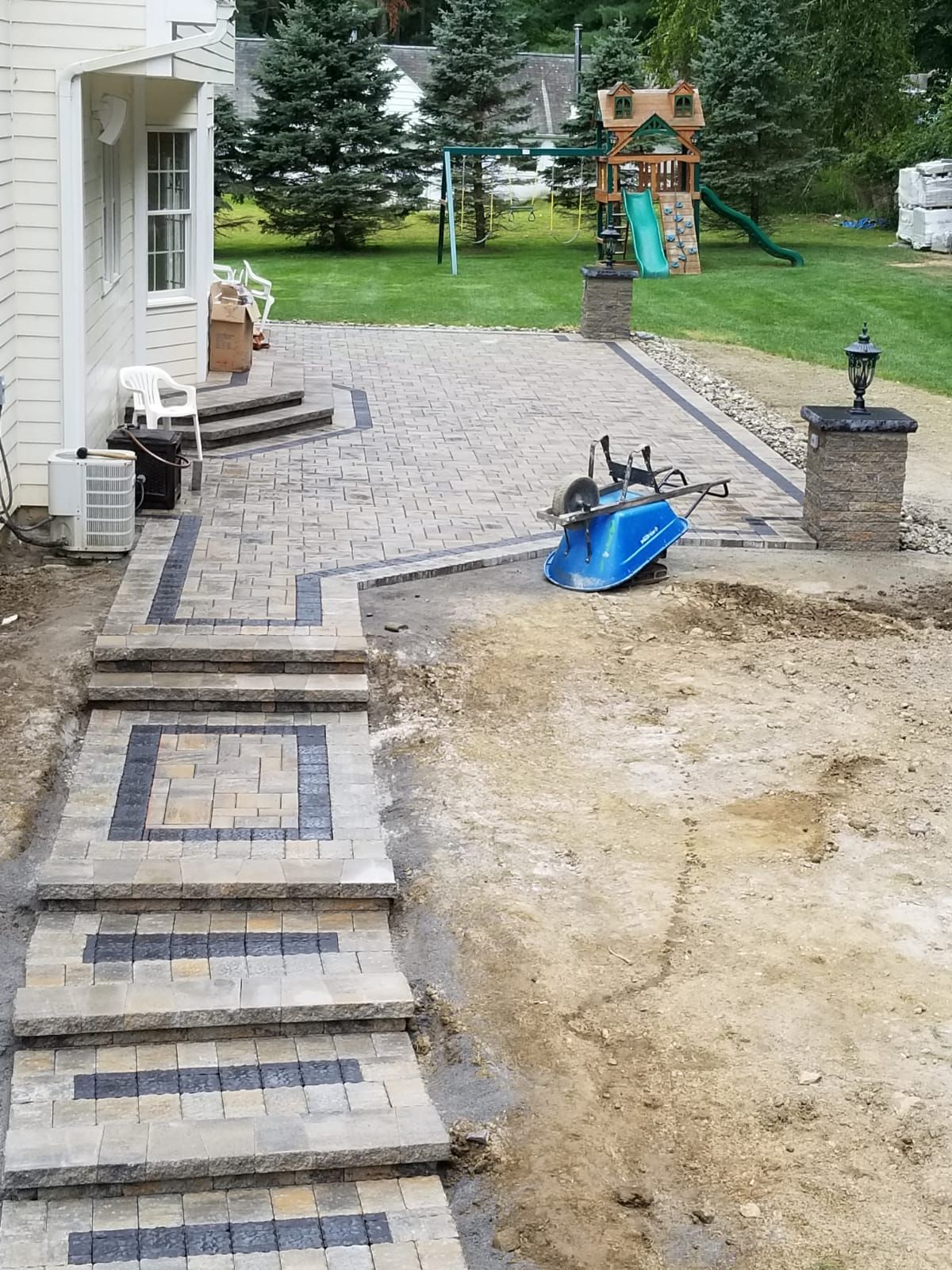A brick walkway is being built in the backyard of a house.