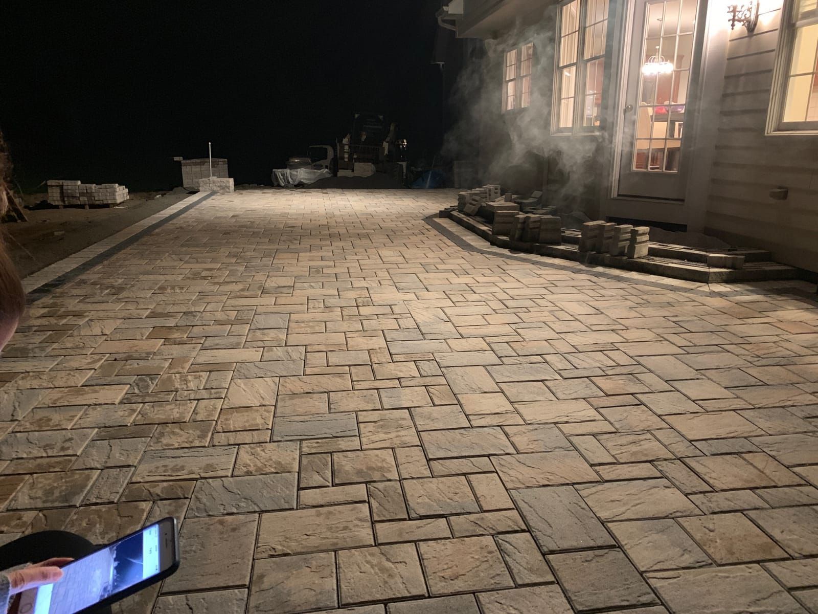 A person is using a tablet on a brick driveway at night.