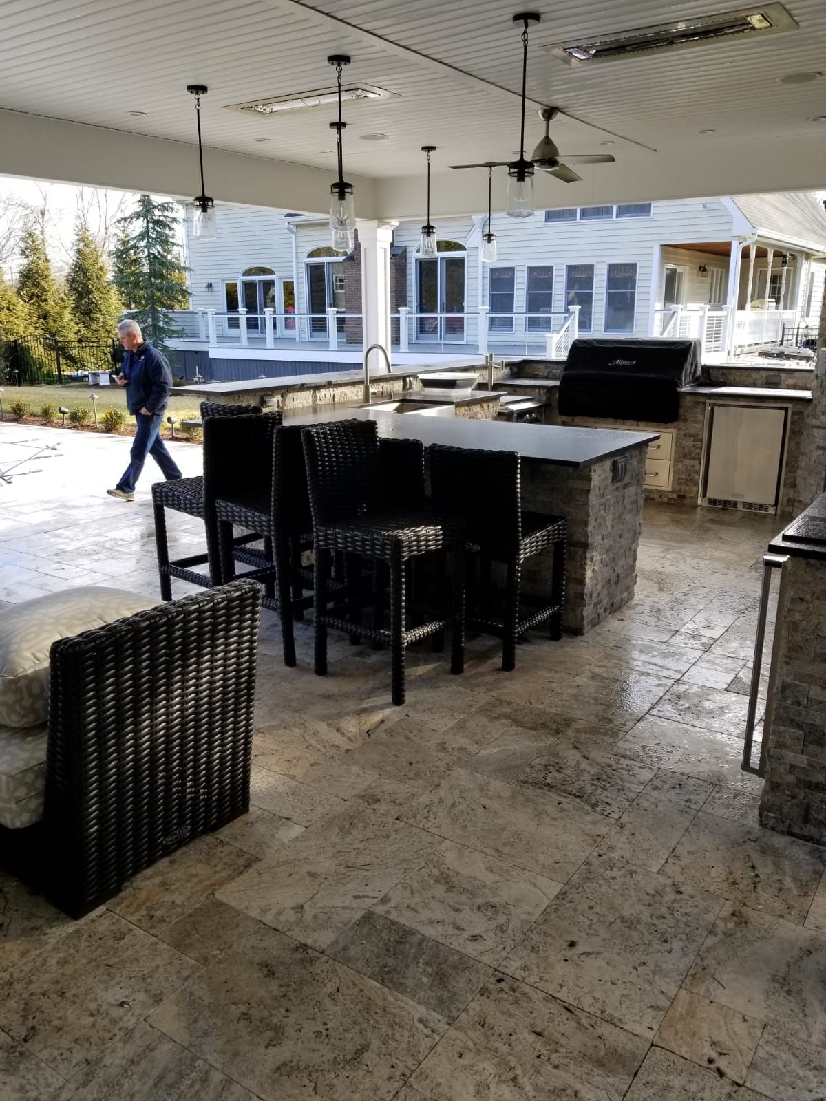 A man is walking in a patio area with a table and chairs.