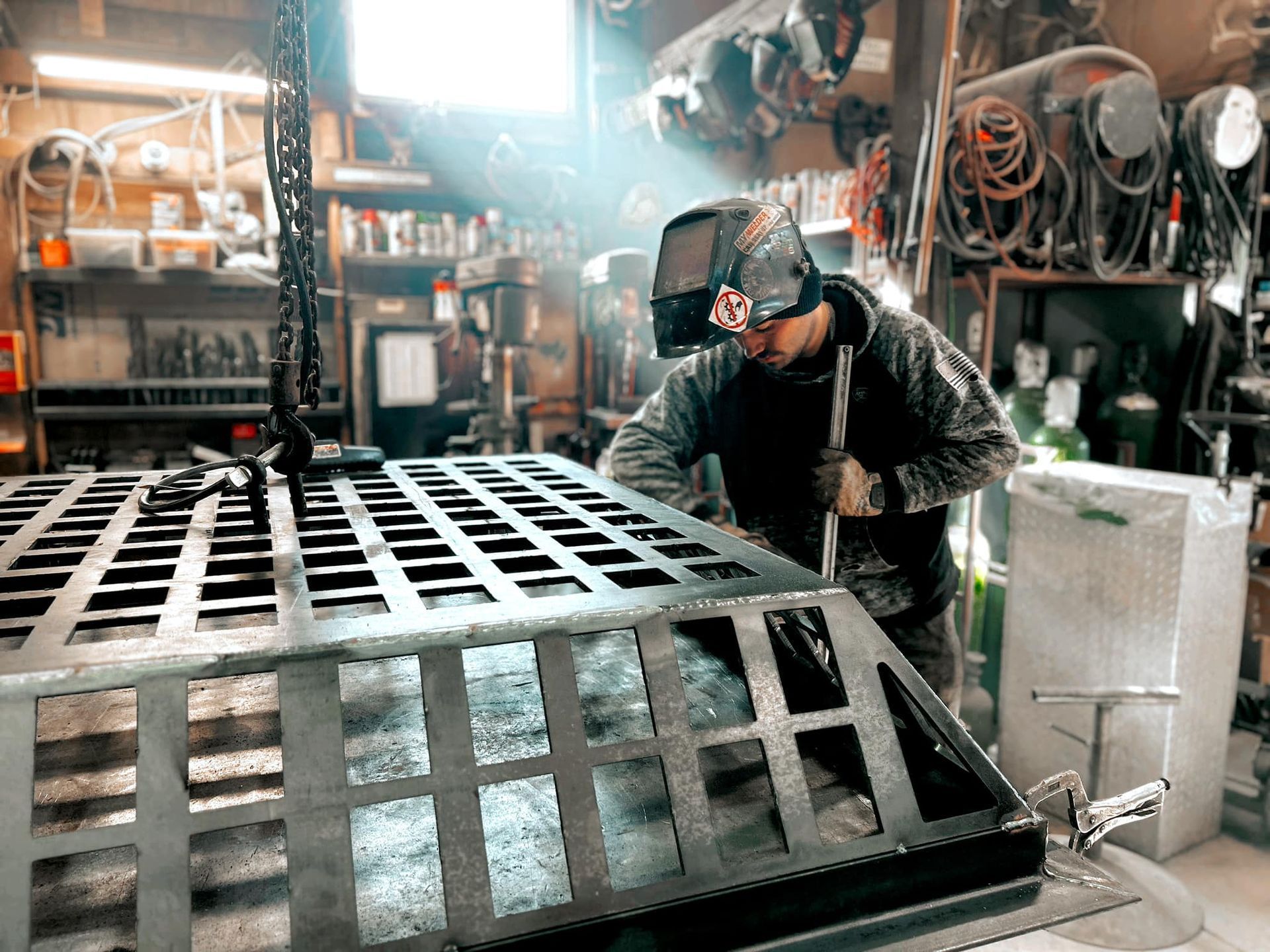 A welder in a workshop, welding a metal grate.