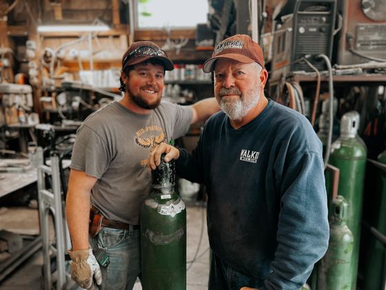 Two men, one young, one older, pose in a workshop.