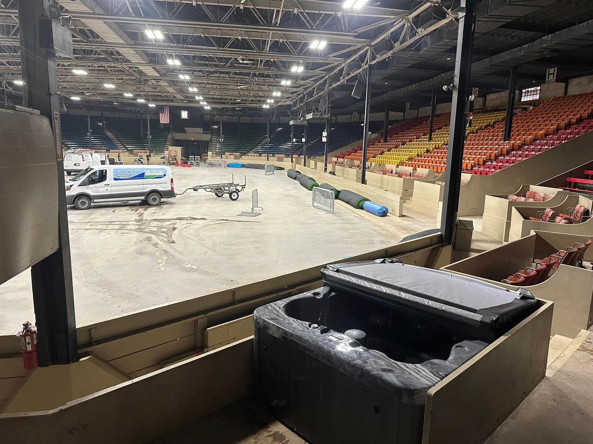 Indoor venue with a hot tub in the foreground, bleachers, and a work van in the background.