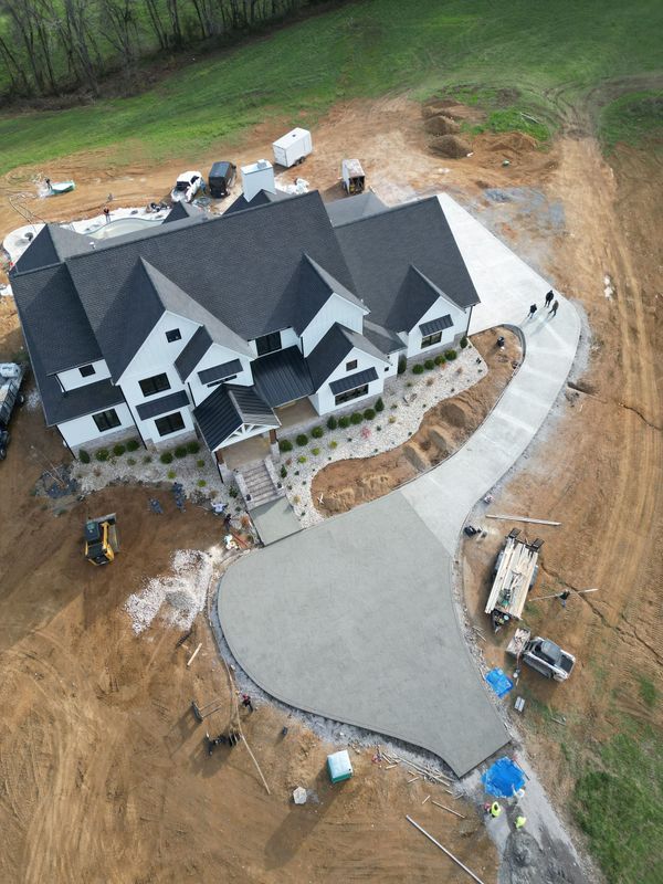 Newly constructed white house with dark roof and concrete driveway; construction site.