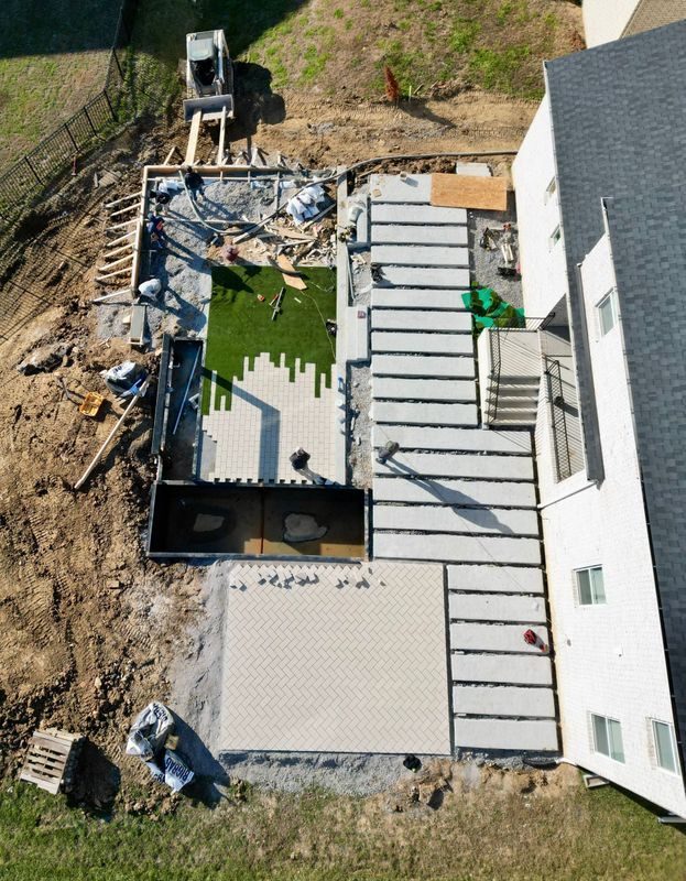 Aerial view of backyard construction: concrete patio, steps, fake grass, house.