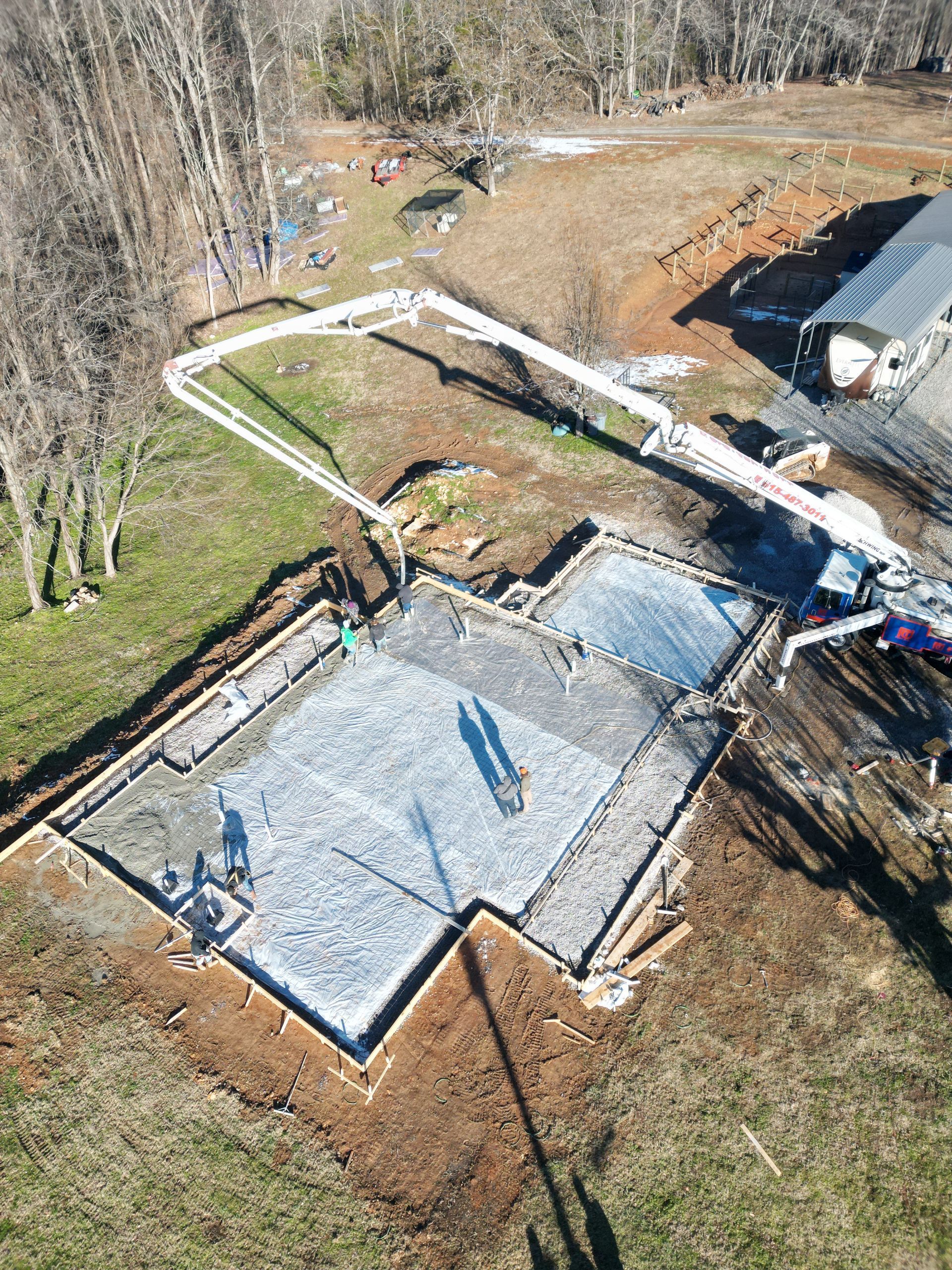 Aerial view of a concrete foundation being poured, with a pump truck extending over the site.