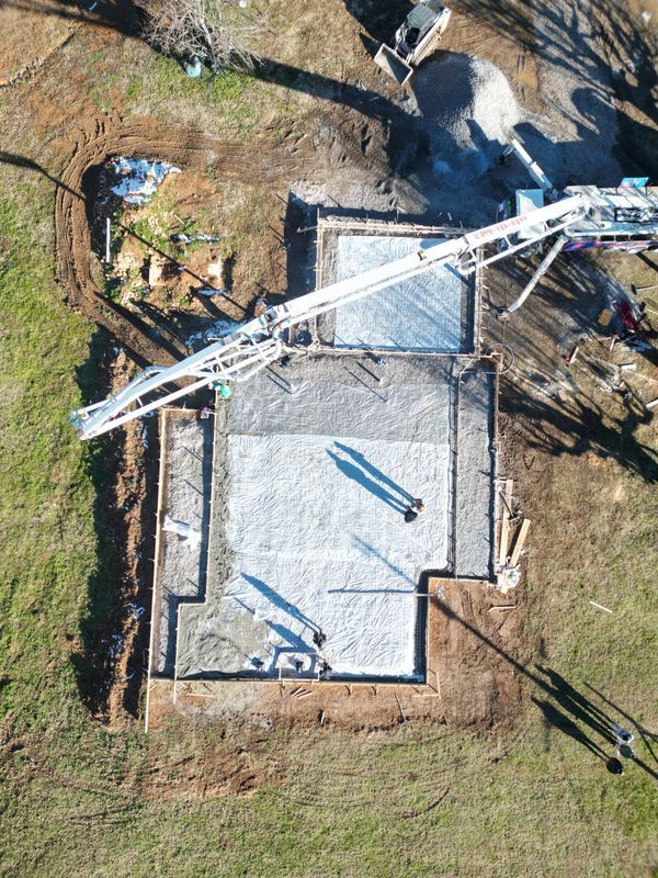 Aerial view of a concrete foundation being poured; construction site with workers, equipment, and a concrete pump.