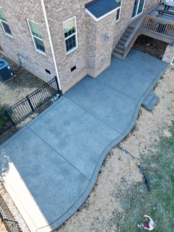 Newly poured concrete patio next to a brick house, featuring a curved edge.