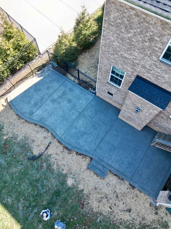 Concrete patio next to a brick house. Uneven edge, steps, and gray color are visible.