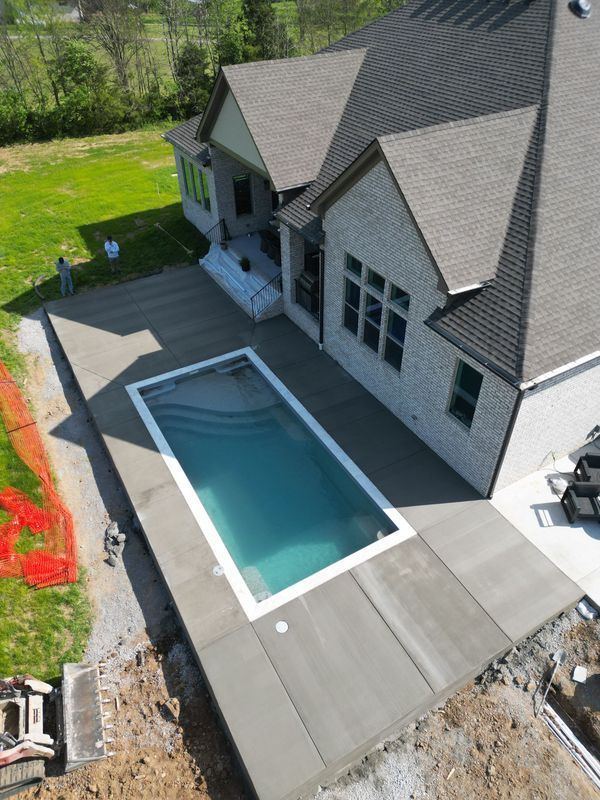 Newly constructed house with rectangular pool and concrete patio.