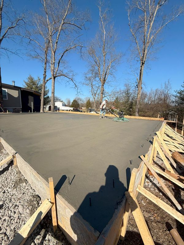 Freshly poured concrete slab in wooden frame, trees in the background, sunny day.